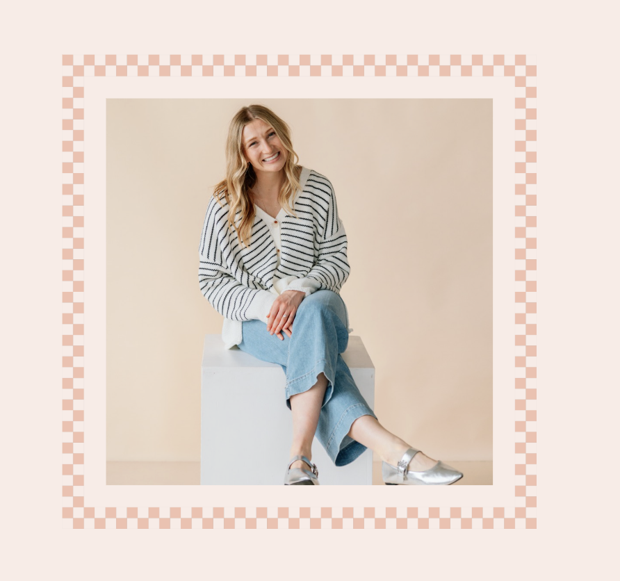 A smiling woman with long blonde hair, wearing a striped sweater, light blue jeans, and silver shoes, sitting on a white block against a plain beige wall.