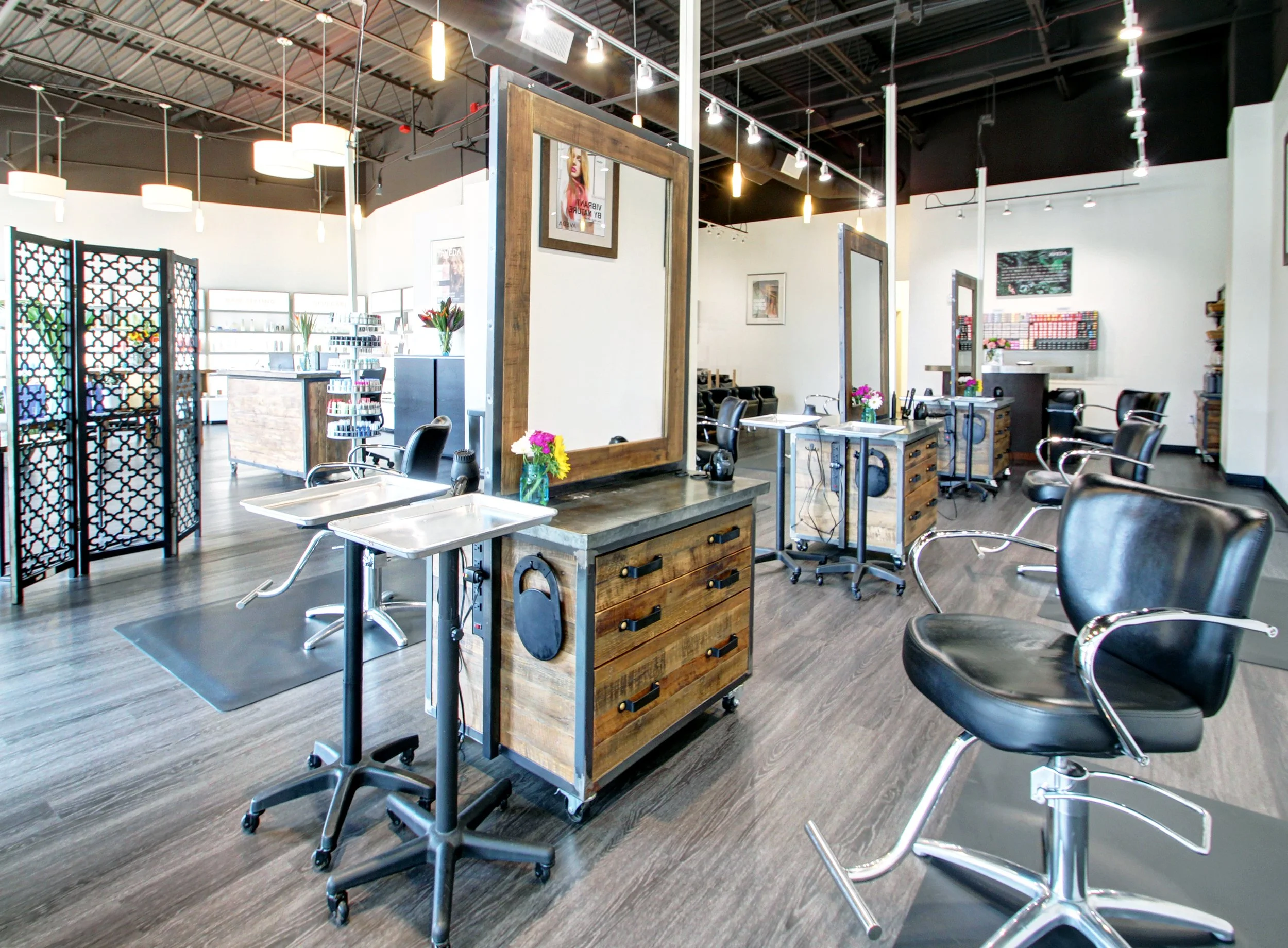 Beauty salon interior with styling chairs, mirrors, and hair stations, decorated with flowers and artwork