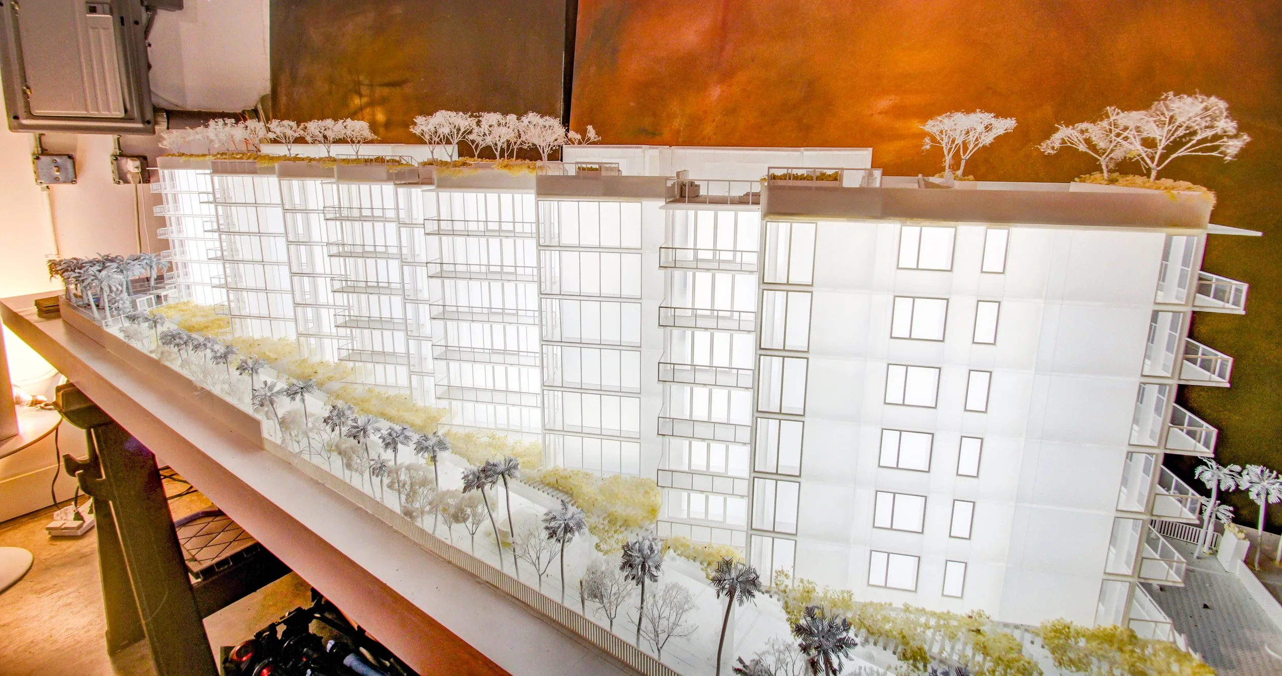 Architectural model of a modern multi-story residential building, featuring balconies, a landscaped rooftop with trees, and a landscaped ground with trees and pathways.