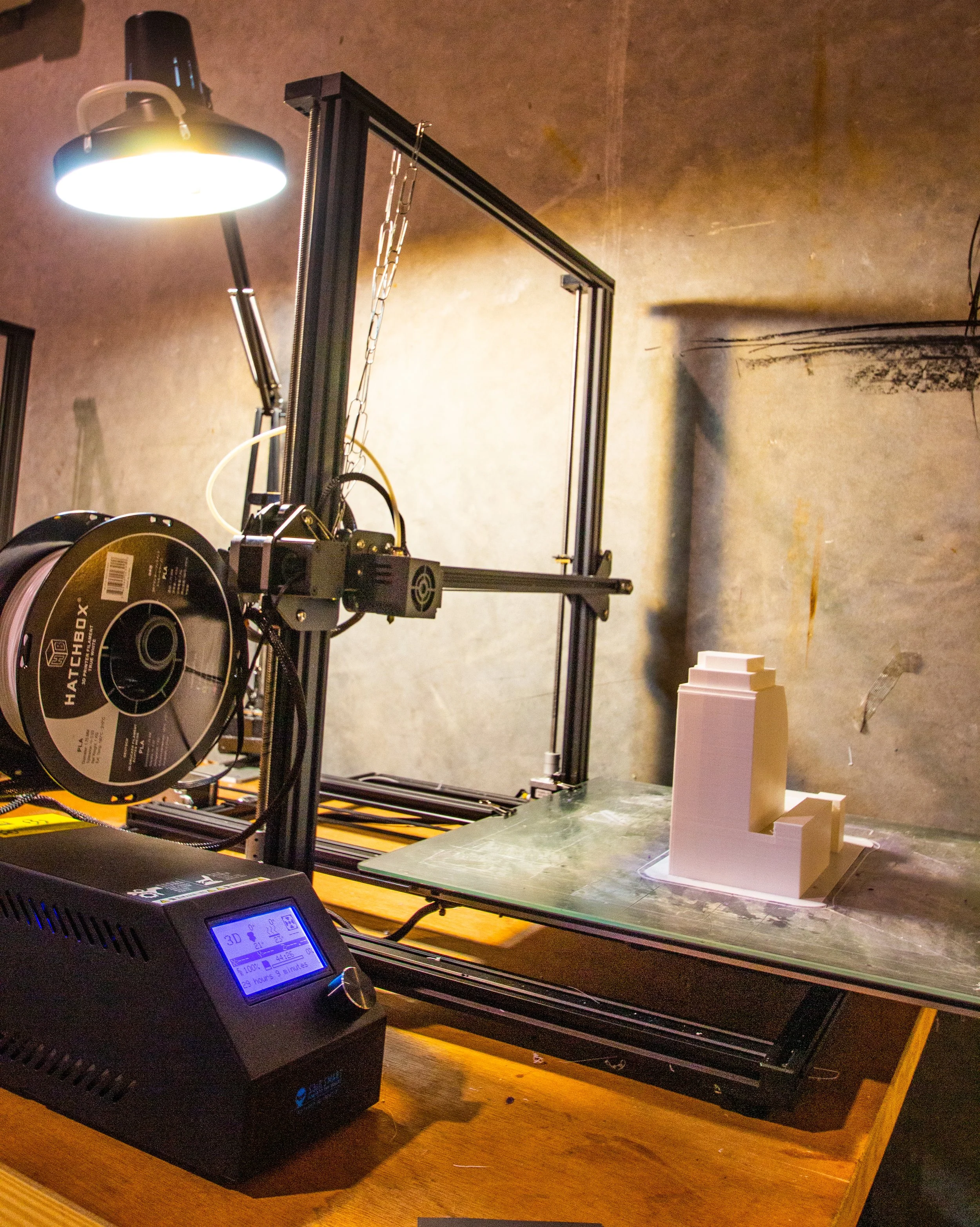 A 3D printer on a wooden table printing a multi-tiered white model.