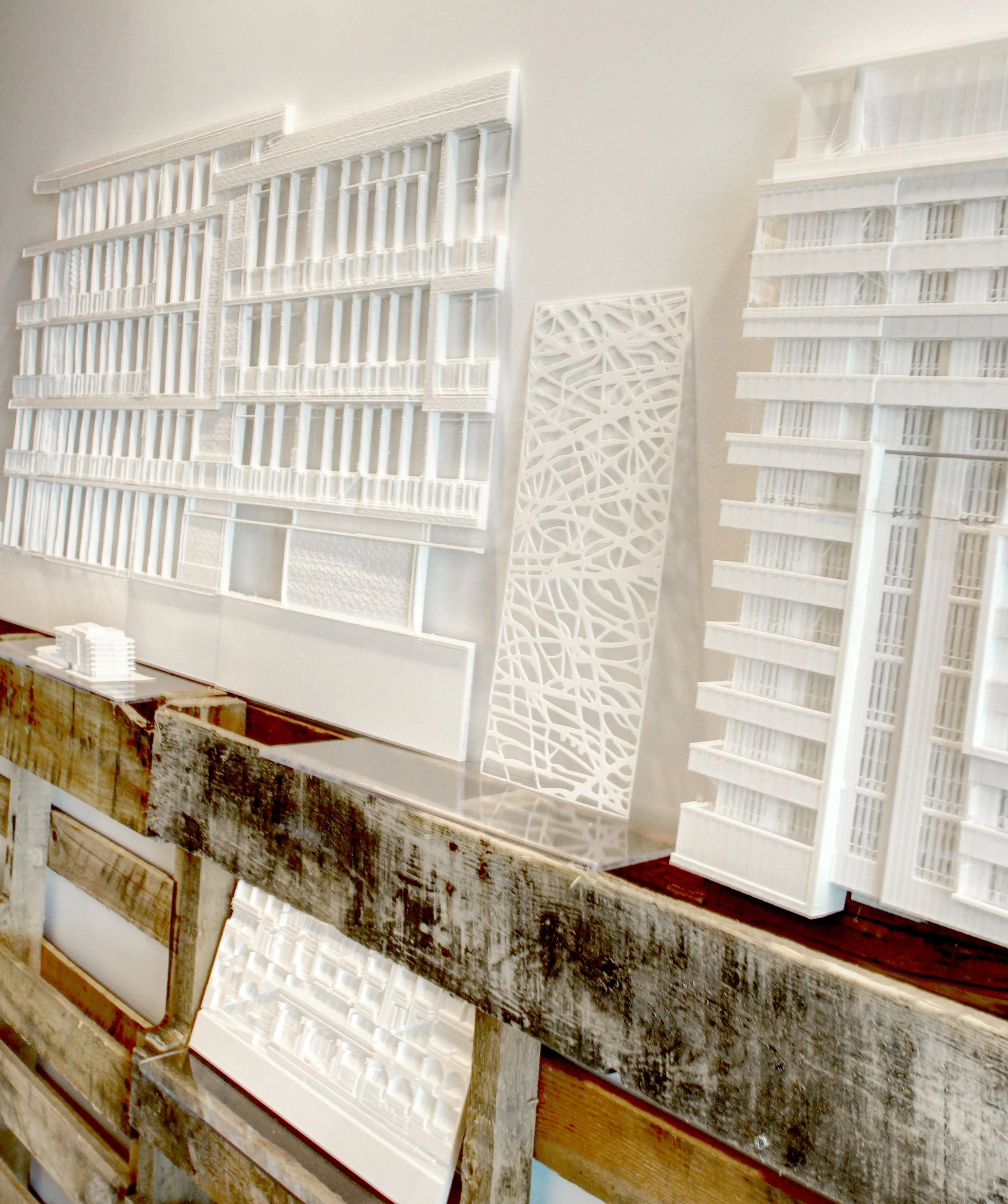 Architectural models of modern white multi-story buildings on a wooden table.