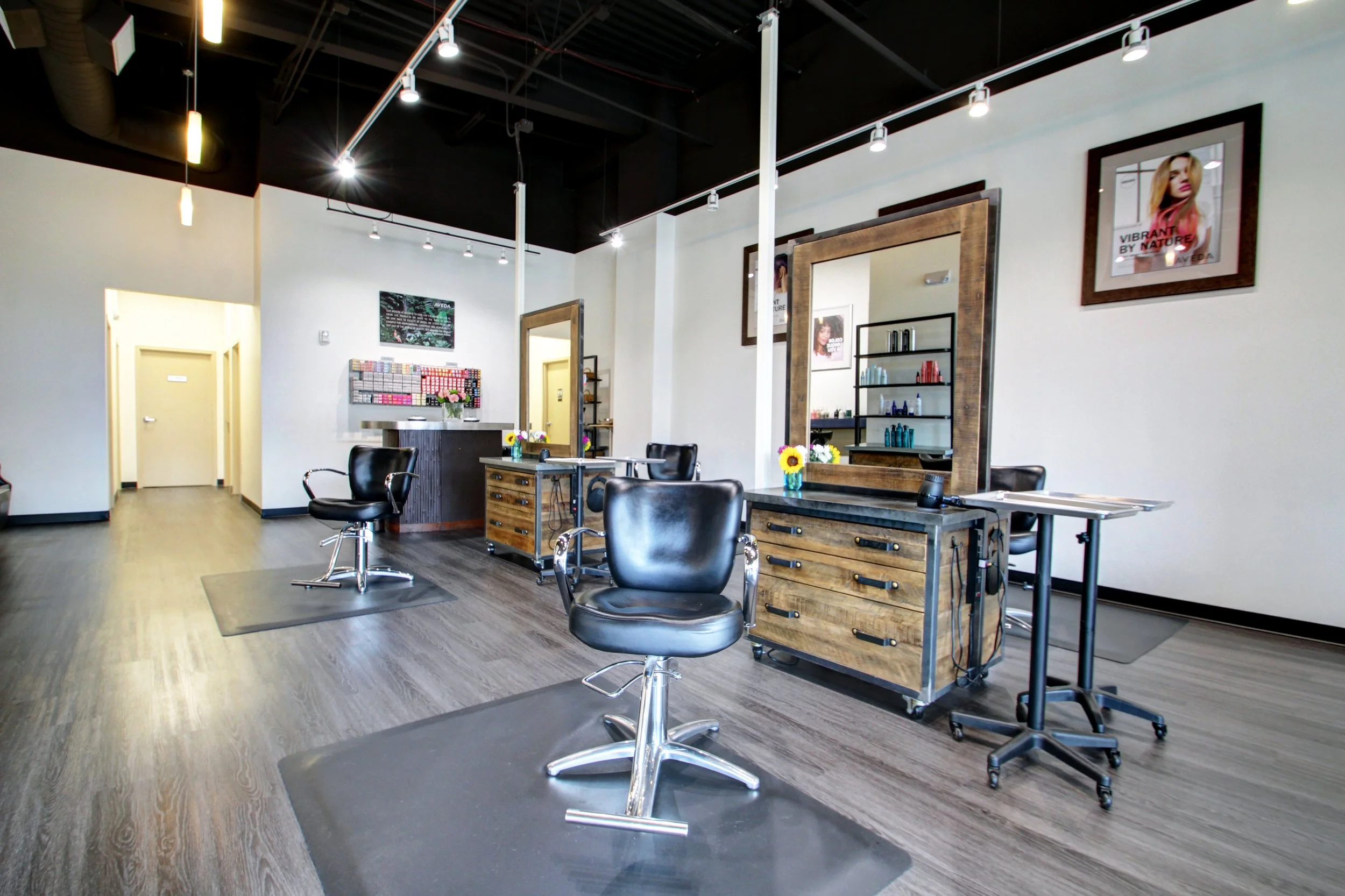 Modern hair salon interior with styling chairs, large mirrors, wooden furniture, and wall art.