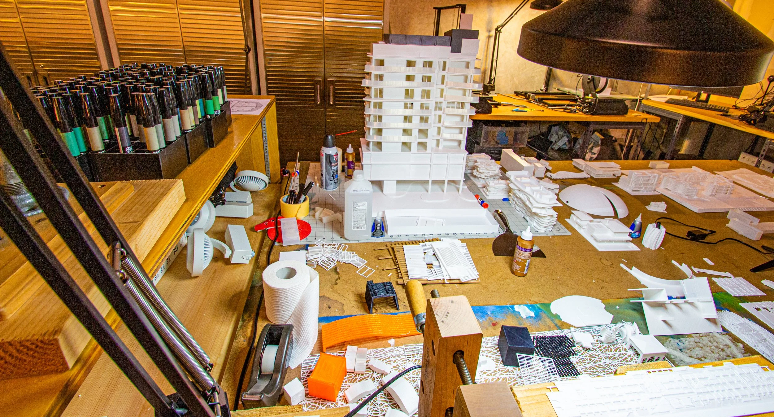 Worktable with architectural models, crafting tools, and supplies in a workshop or design studio.