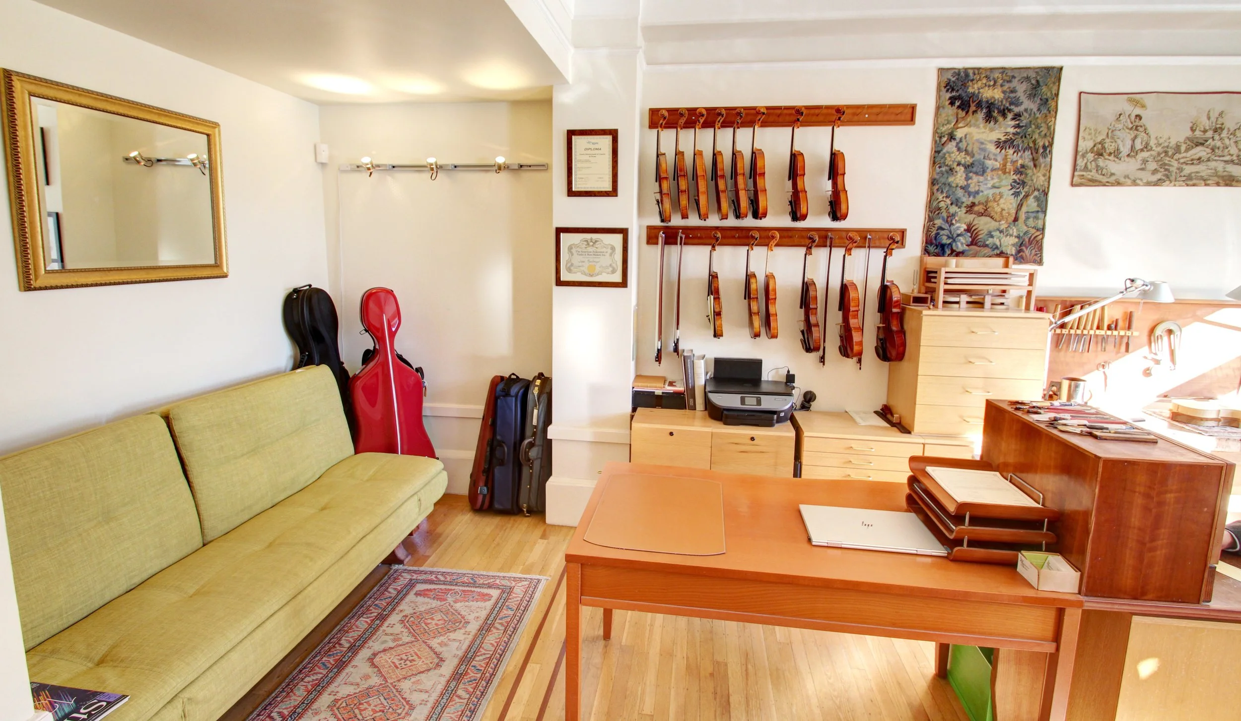 A music shop with a yellow couch, guitar cases, and a display of violins hanging on the wall.