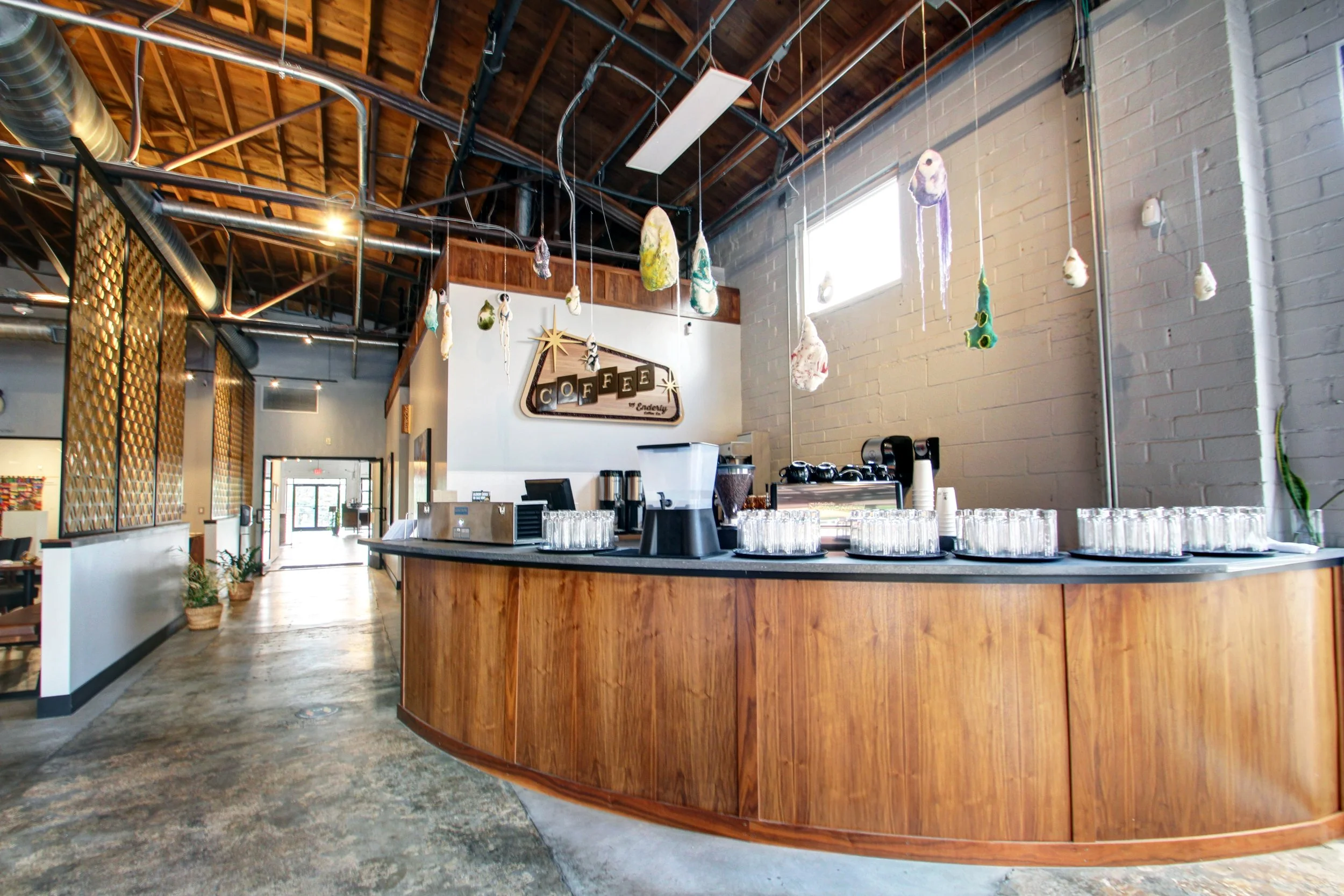 Interior of a coffee shop with a curved wooden counter, hanging colorful decorations, and a sign that says 'Coffee'.