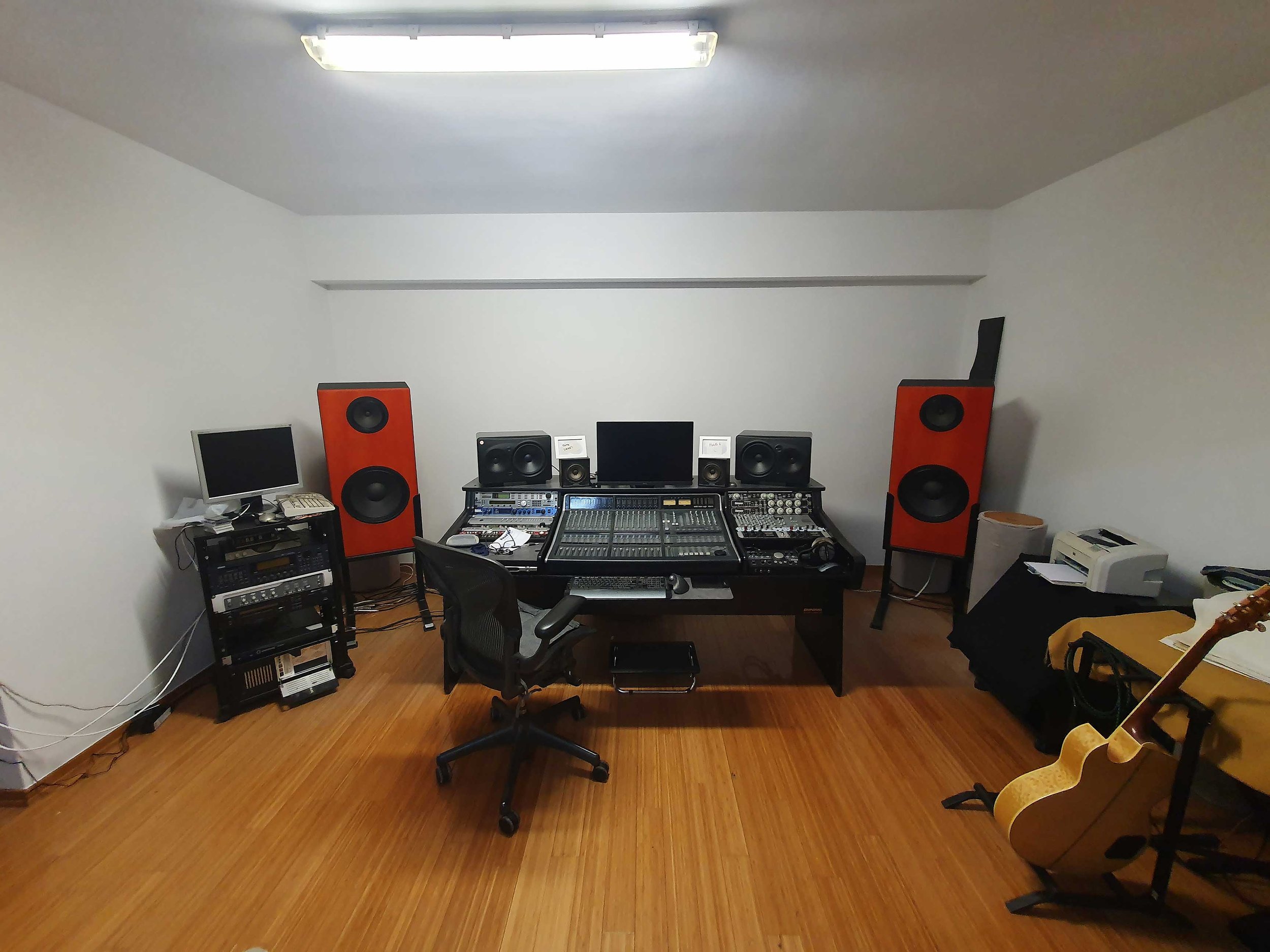 Recording studio with large orange speakers, computer, mixing console, and musical instruments on the right side.