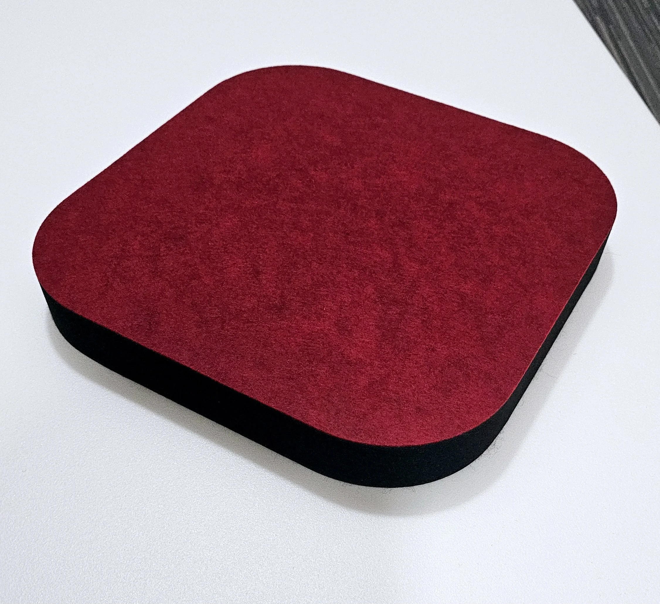 A square device with rounded edges, red top surface, and black sides, placed on a white surface.