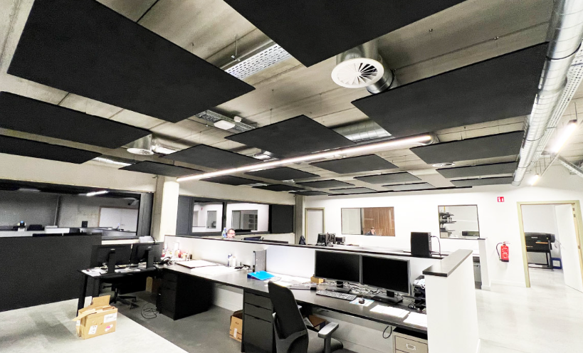 Office workspace with multiple desks, computers, and black acoustic panels on the ceiling.