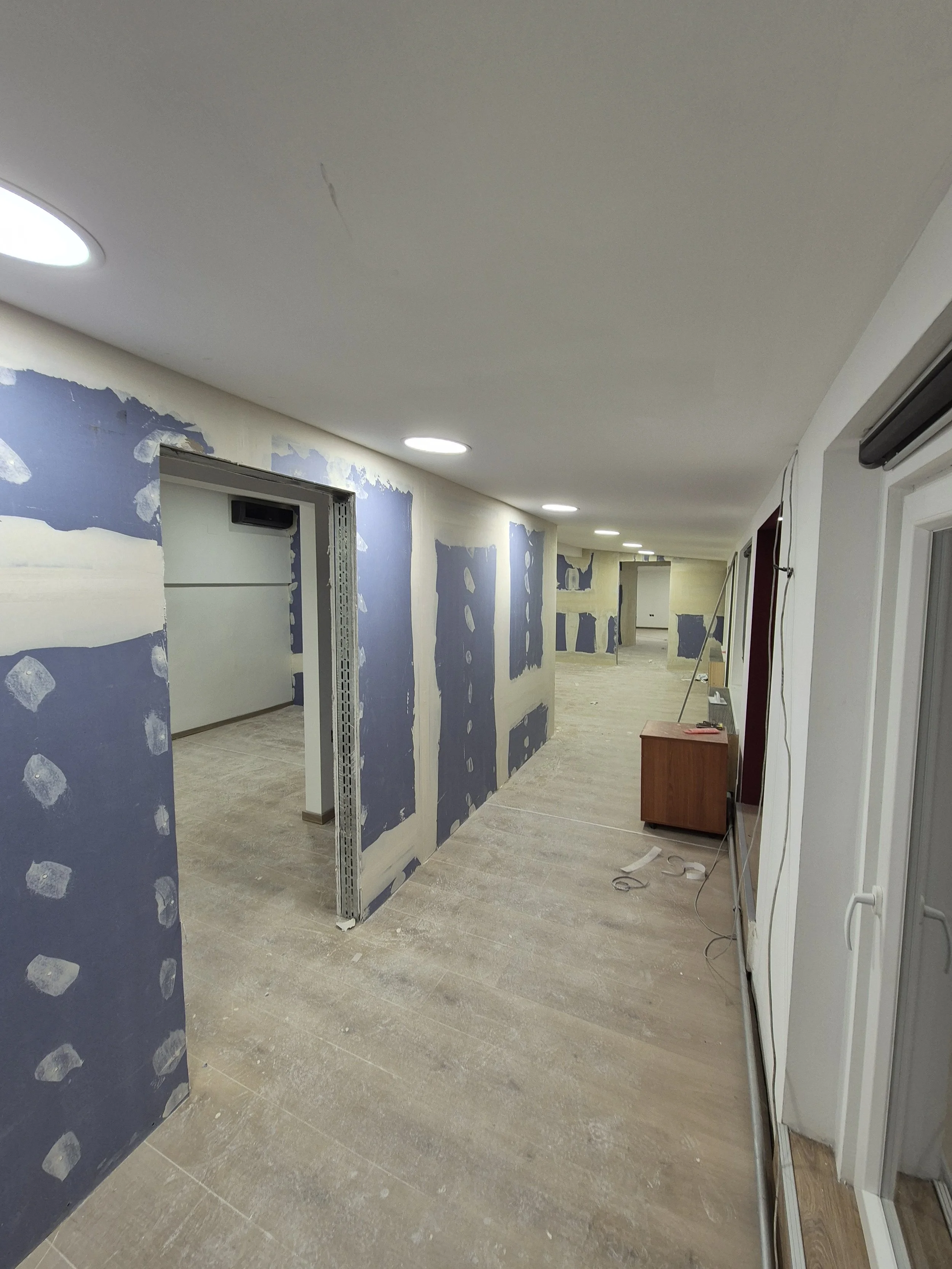 Interior of a building under renovation with drywall in progress, visible blue drywall joint compound, and construction tools on the floor.