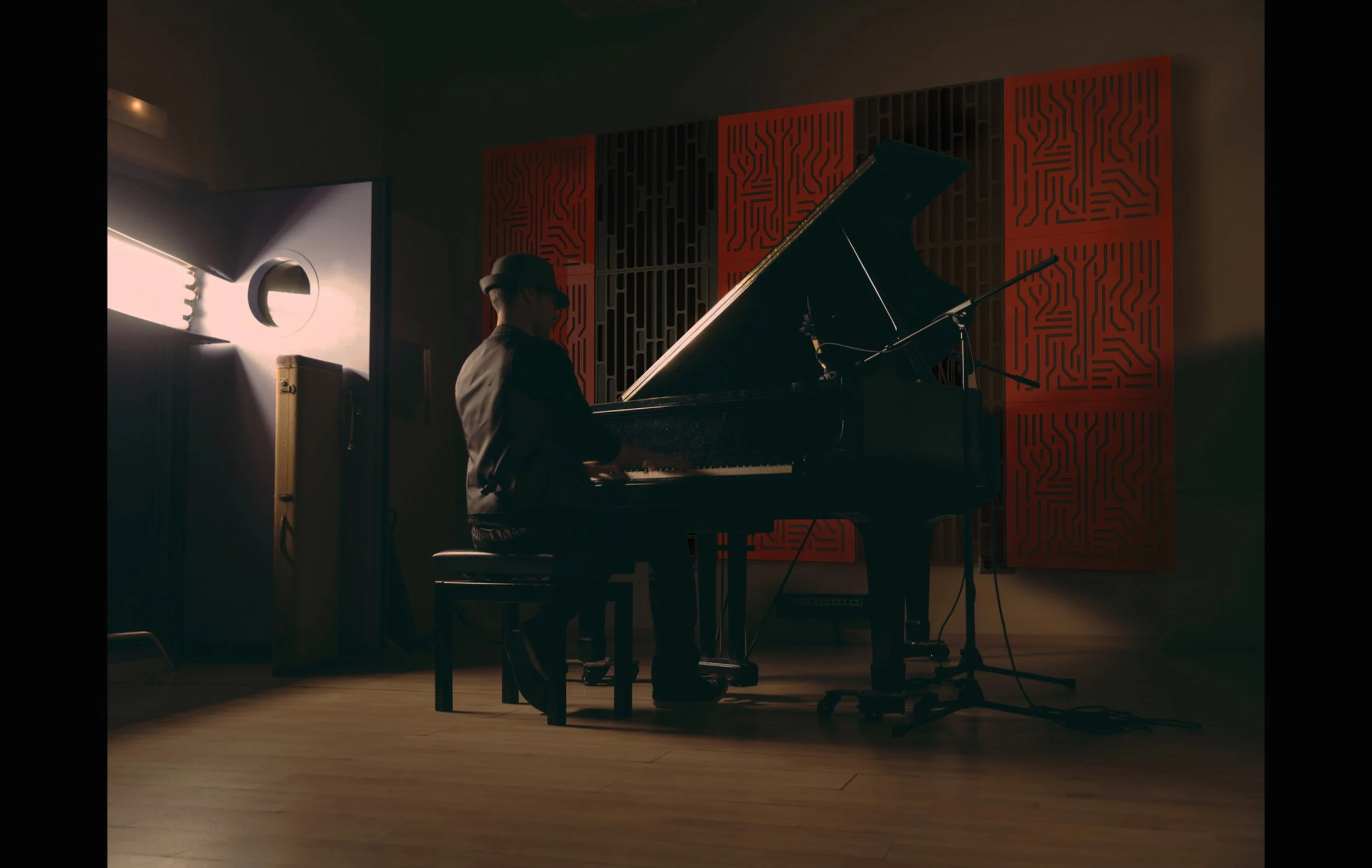 Person playing grand piano in a dimly lit music studio with soundproofing panels on the wall.