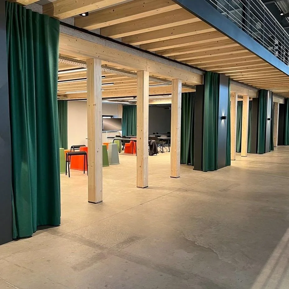 Modern interior space with wooden beams, green curtains, chairs, and desks, possibly a conference or meeting area.