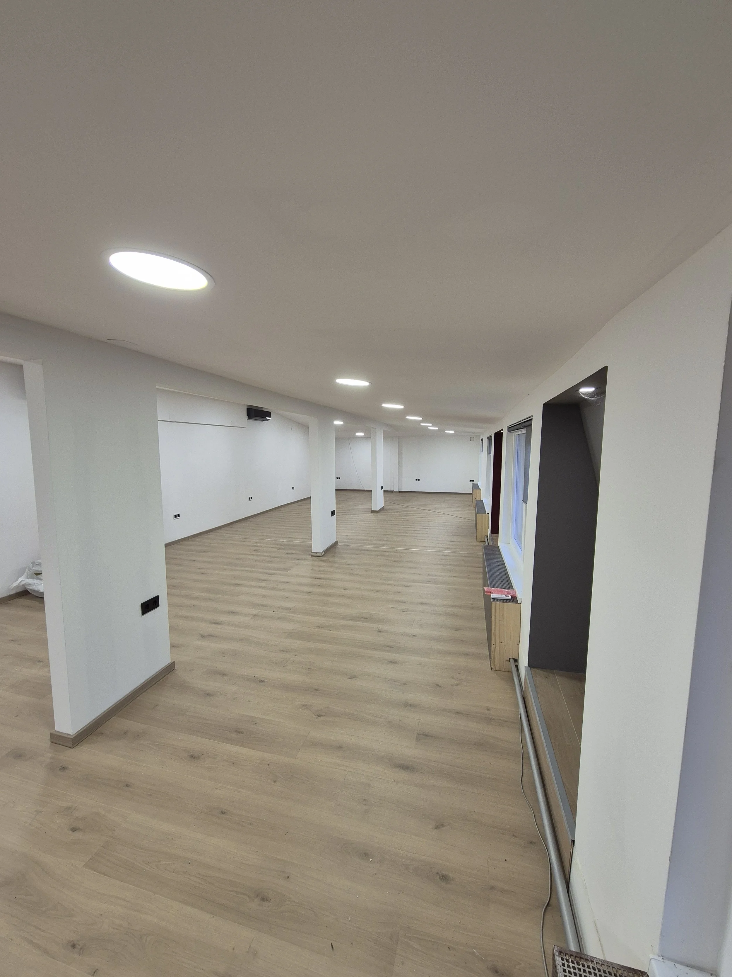 Empty interior room with white walls, wooden flooring, and ceiling lights.