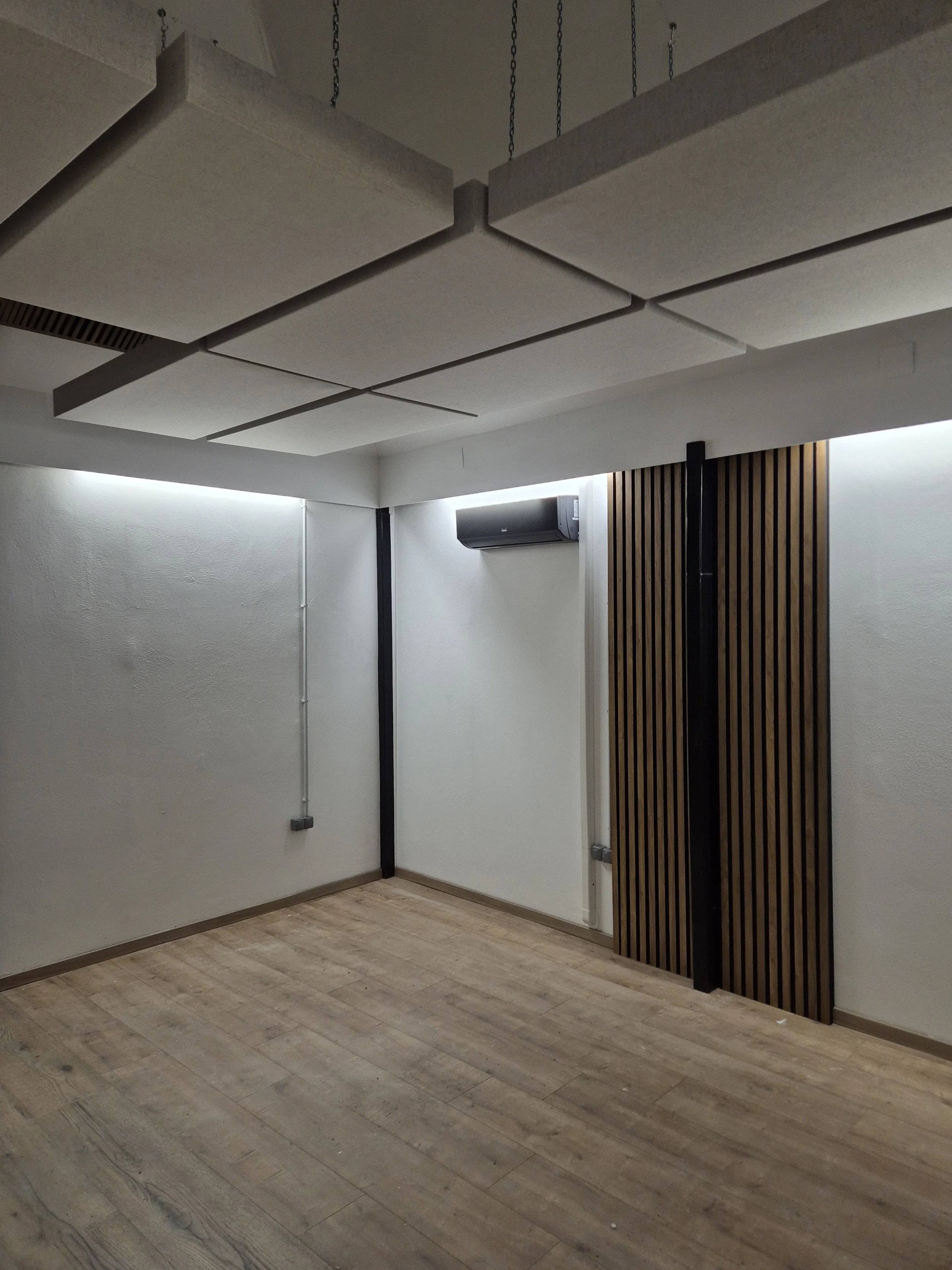 Empty room with white walls, wood flooring, acoustic panels on the ceiling, and an air conditioning unit on the wall.