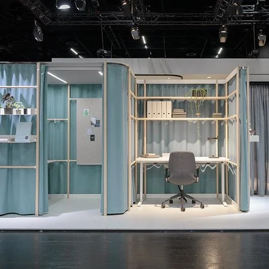 Small modern workspace with a desk, chair, shelves, and a storage area inside a partitioned cubicle.