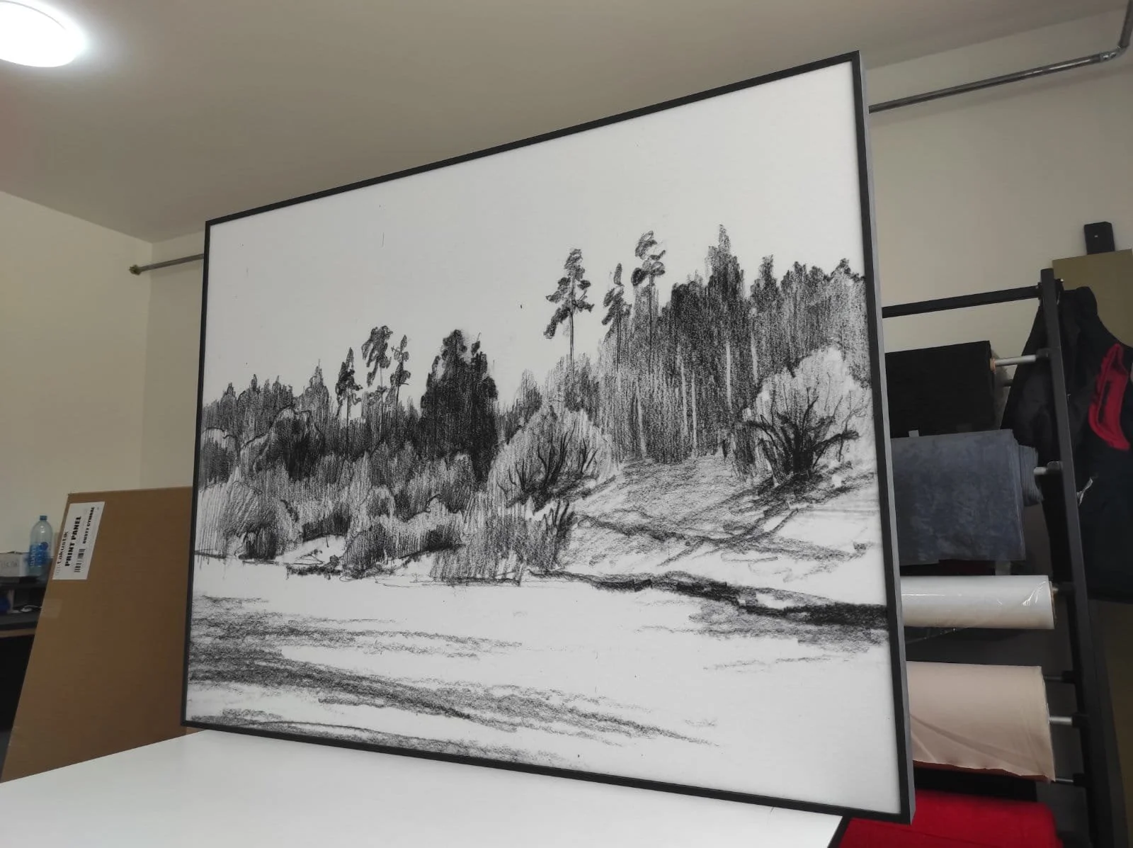 Black and white drawing of a landscape with hills, trees, and a cloudy sky, viewed on a whiteboard or screen in a room.