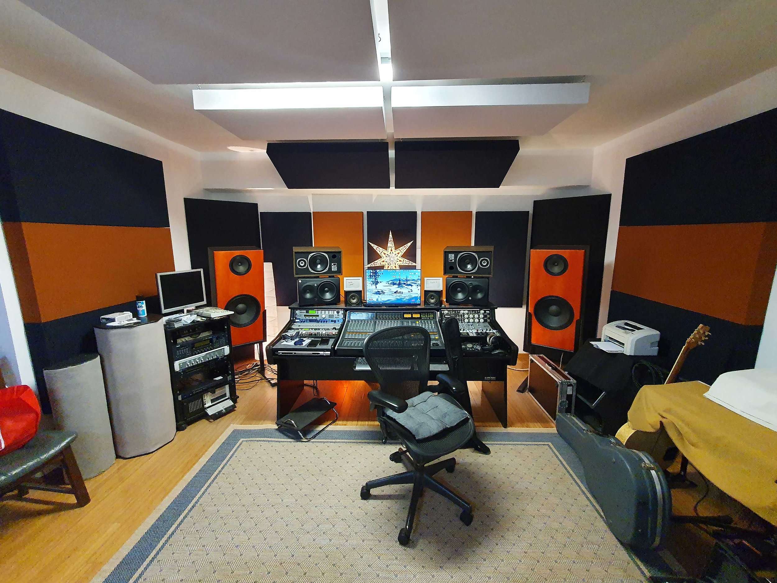 A professional recording studio with large speakers, mixing consoles, and computer monitors.