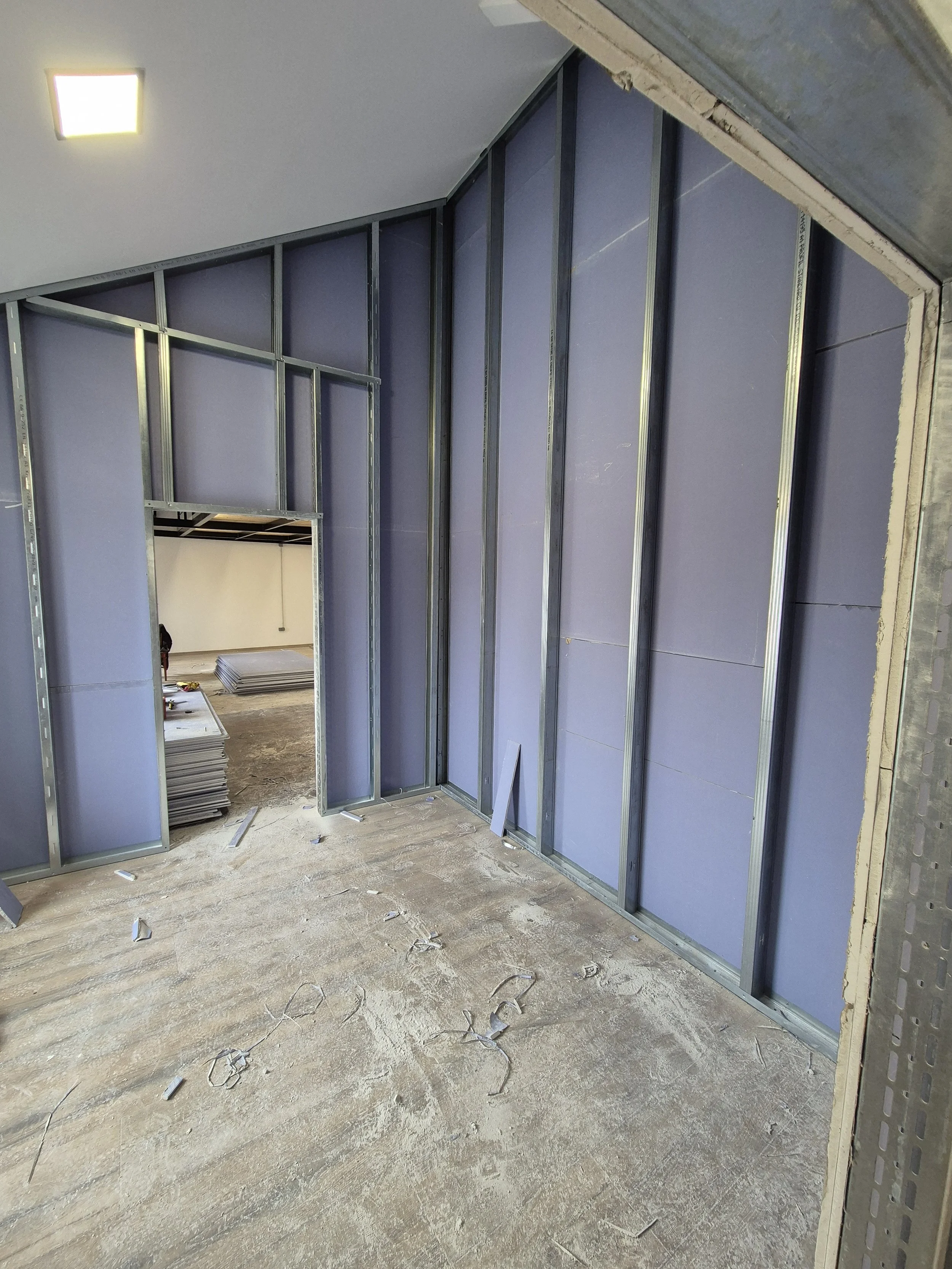 Interior of a room under construction with exposed metal wall studs and purple insulation panels, and a partially finished ceiling.