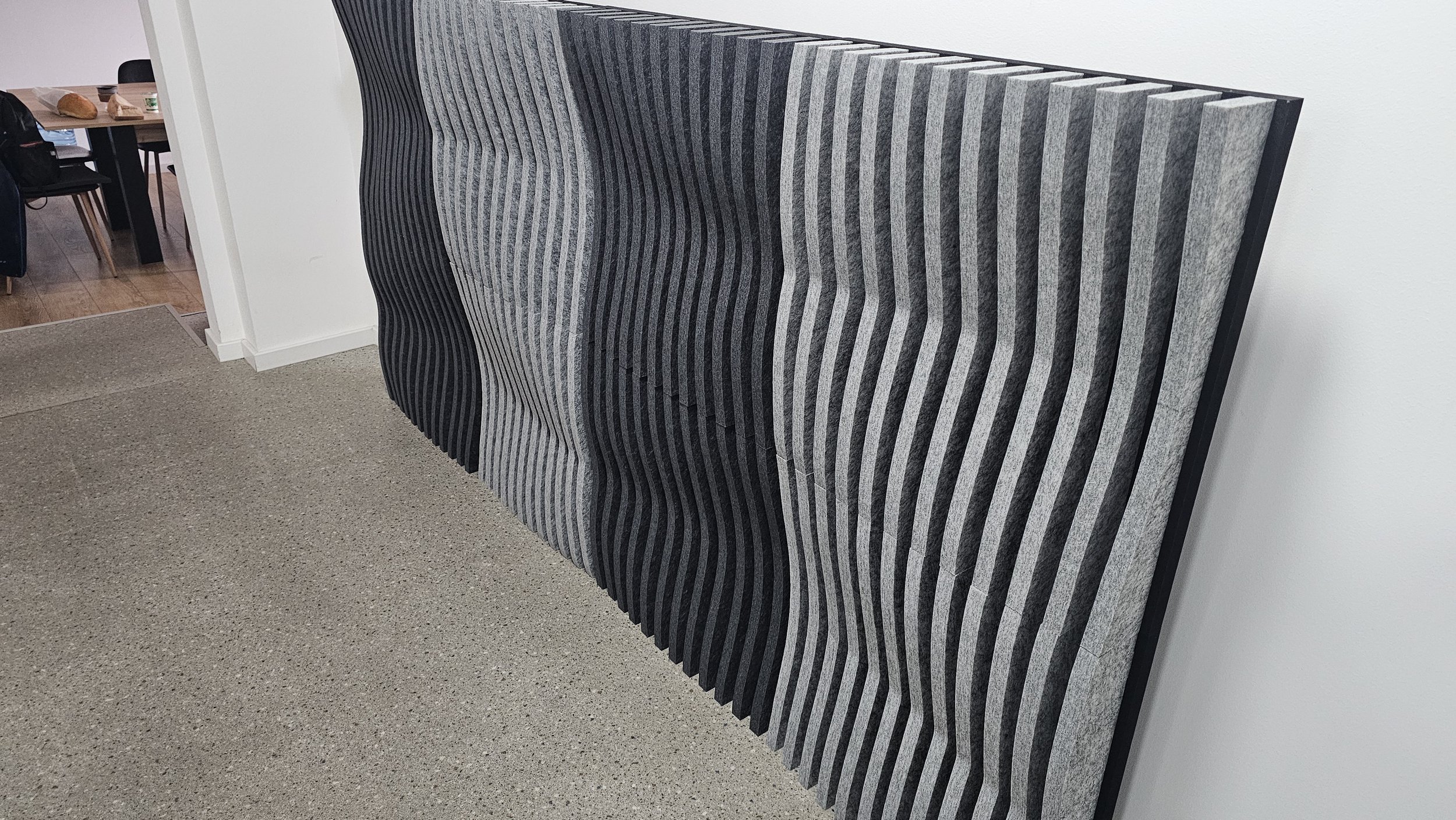 Stacked acoustic wall panels with black and gray wavy striped pattern in an office space.