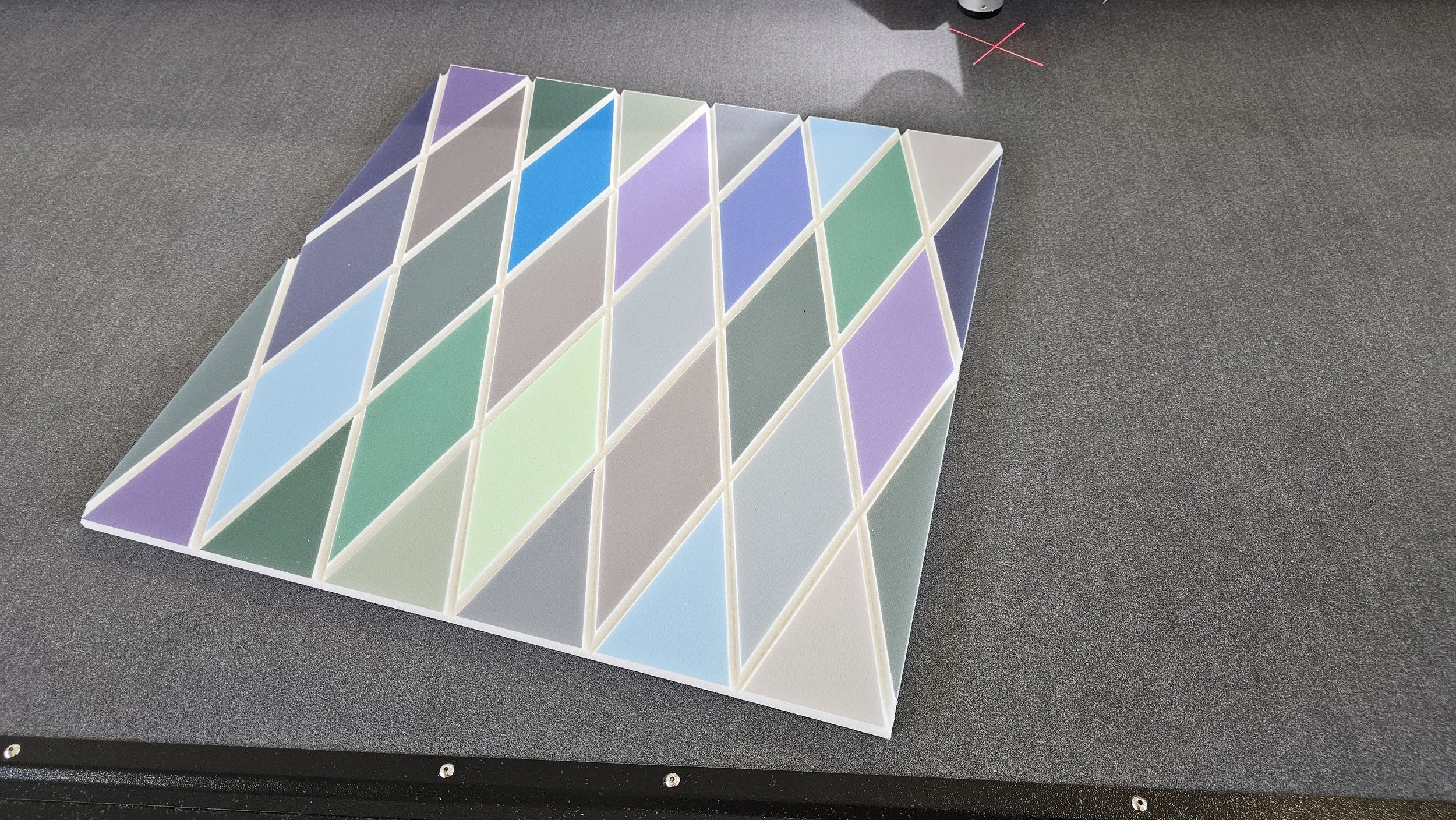 A colorful geometric tile pattern with a series of parallelograms in various pastel shades, arranged in a grid on a black surface.