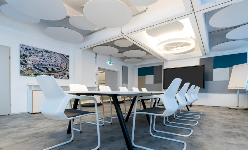 Modern conference room with white and black chairs, a long table, a large screen, a painting, and geometric wall decor