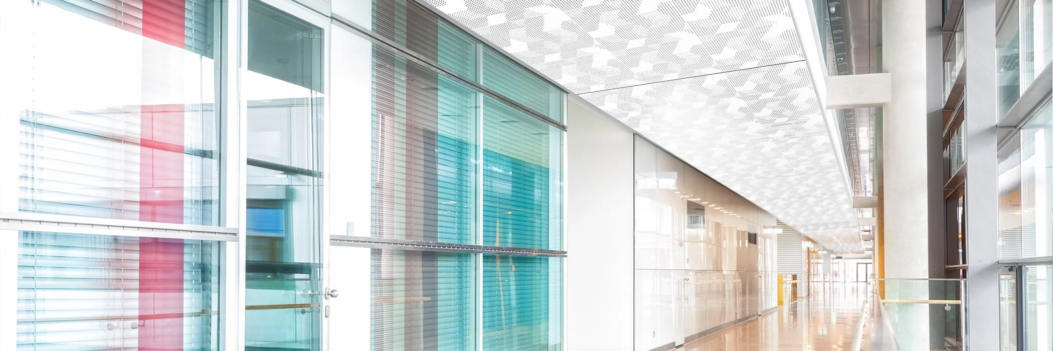 Modern indoor corridor with glass walls, colorful panels, and reflective floors, in a corporate building.