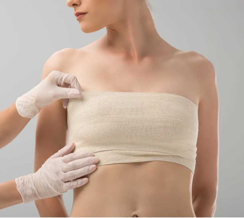 Medical professional adjusting a beige bandage wrap on a woman's chest in a clinical setting.