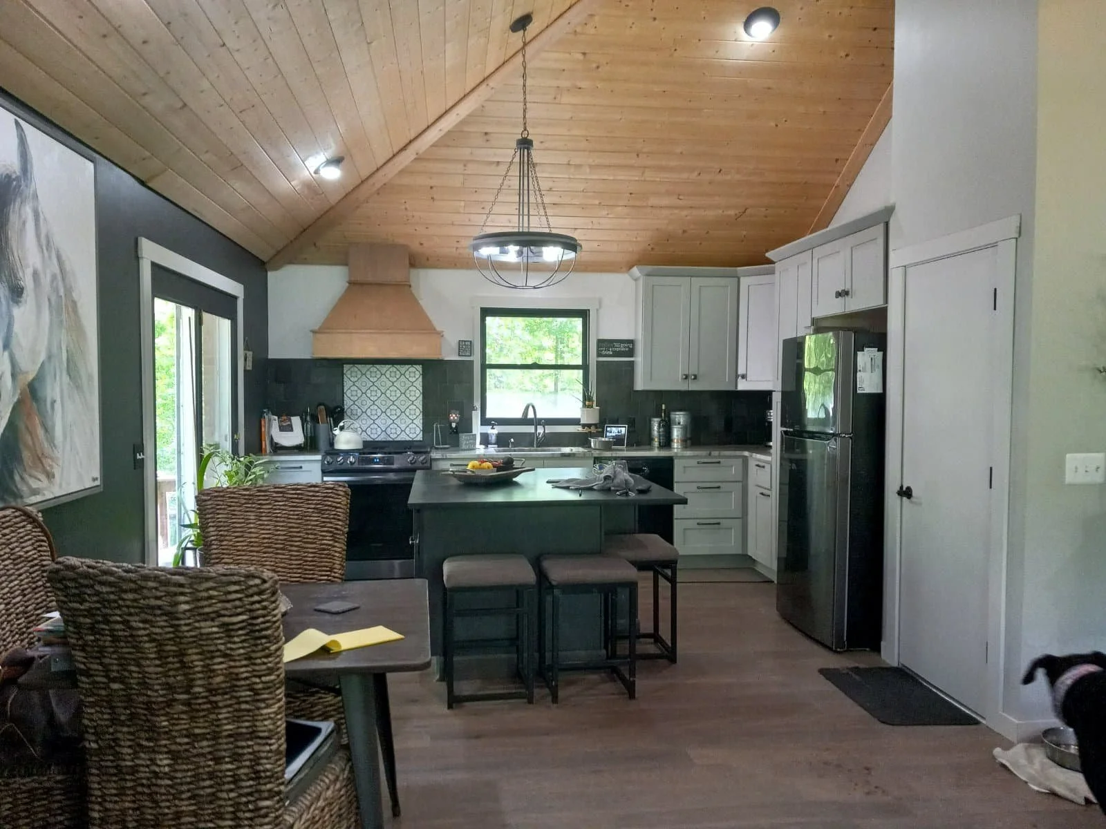 Modern kitchen home renovation design with wooden ceiling, island, stainless steel appliances, dining area, and a dog in the foreground.