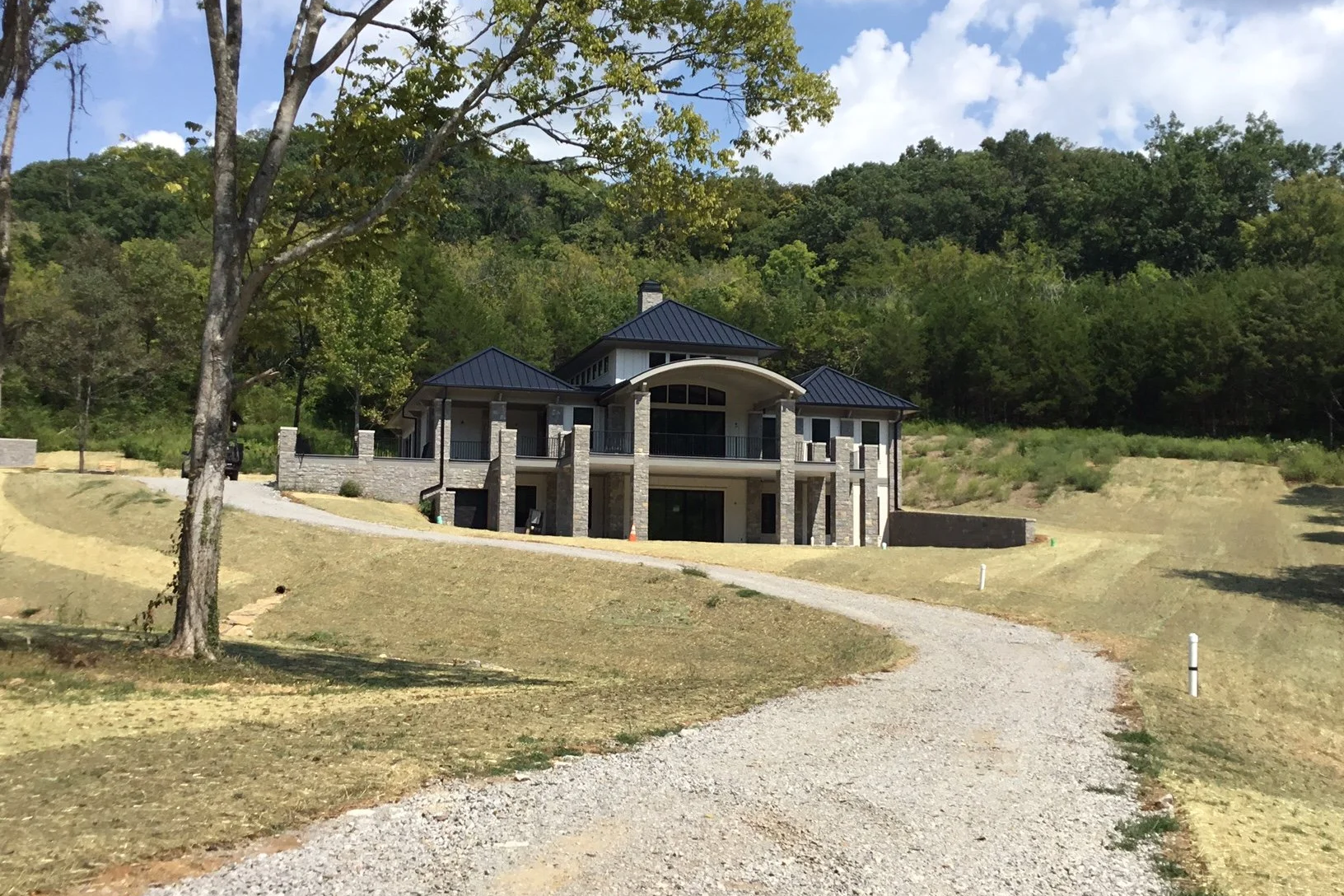 Newly constructed house on a hill with a gravel driveway, surrounded by green trees and a partly cloudy sky with  custom kitchen design with cabinetry by Few Oaks