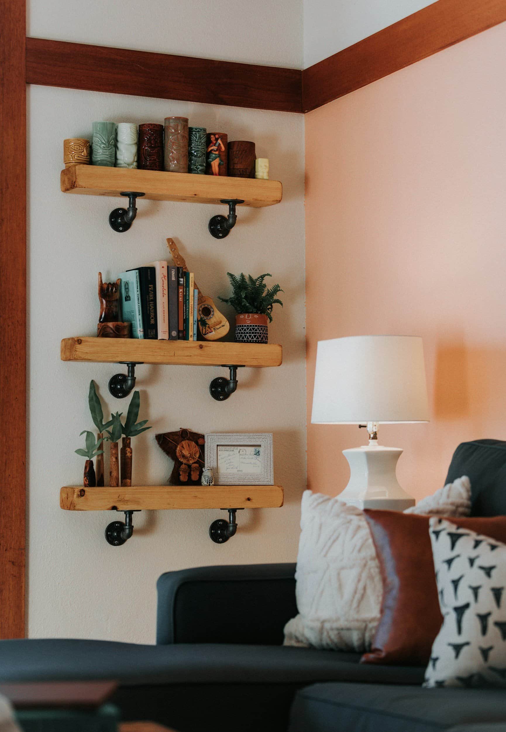 Three wooden wall shelves with decor, books, and plants—perfect for stylish rental property design above a cozy couch and lamp.