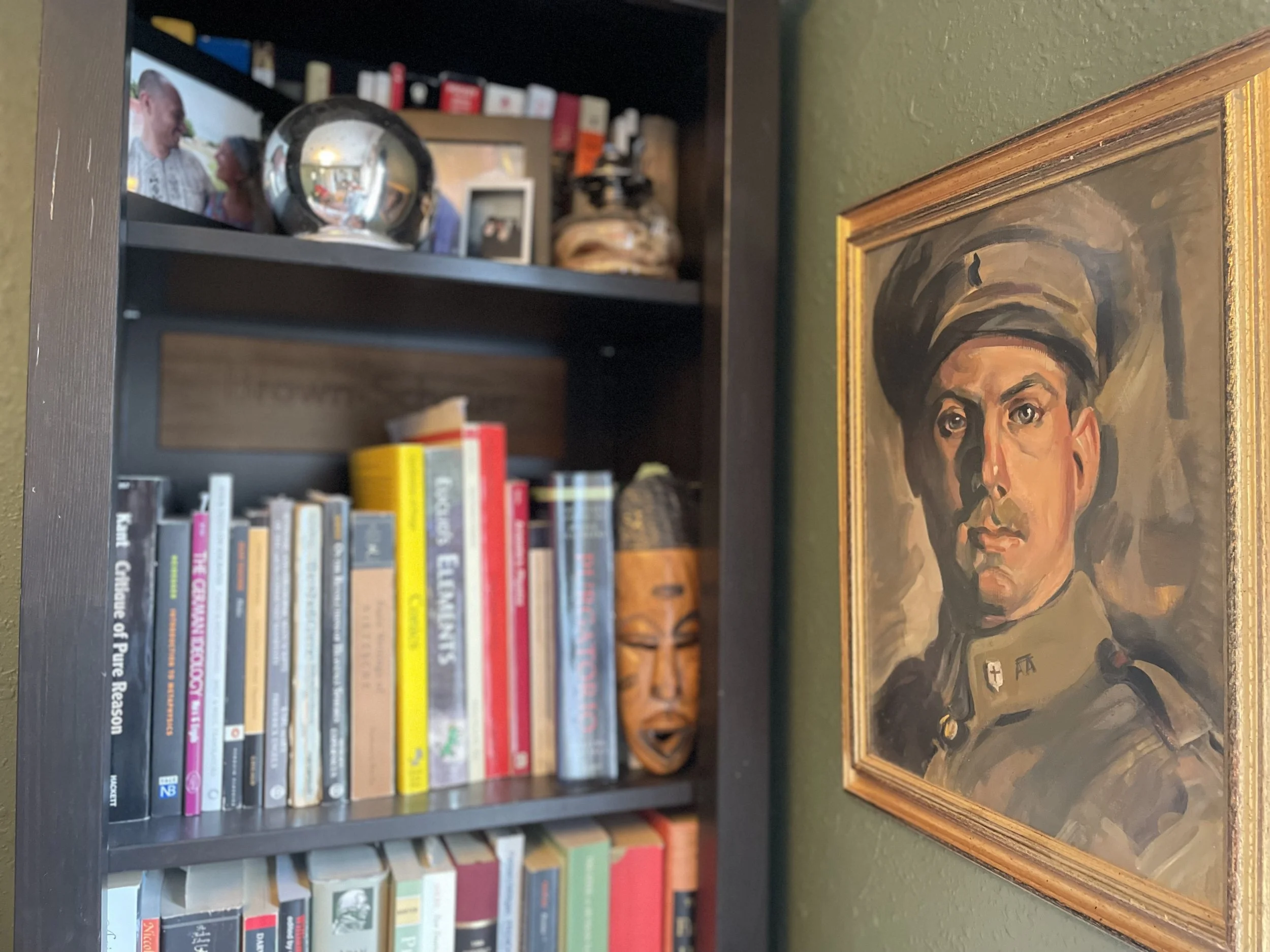 A portrait painting of a man in military uniform on a green wall, with a bookshelf filled with books and decorative items behind it.