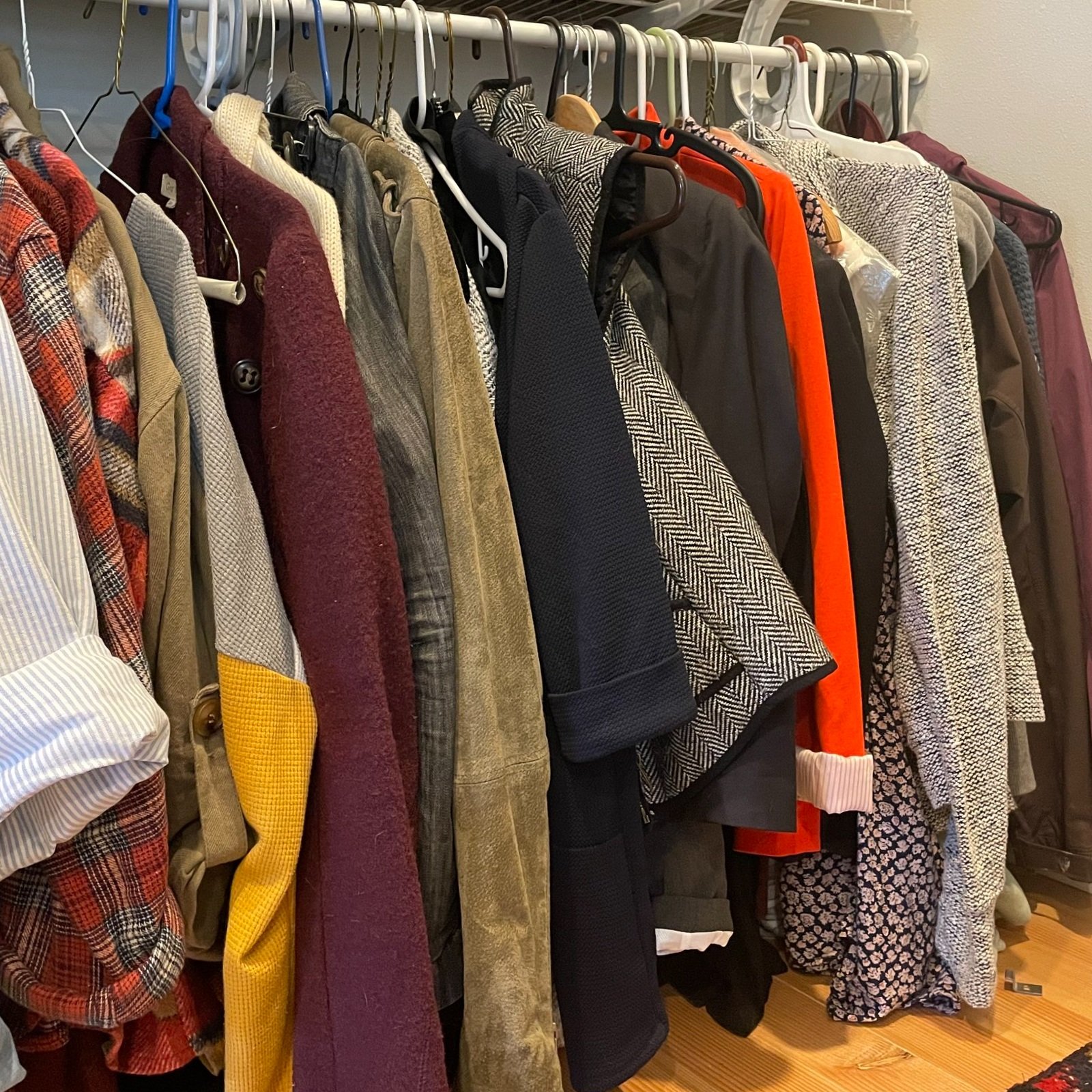Clothes hanging on a rack in various styles and colors, including jackets, blazers, and coats.