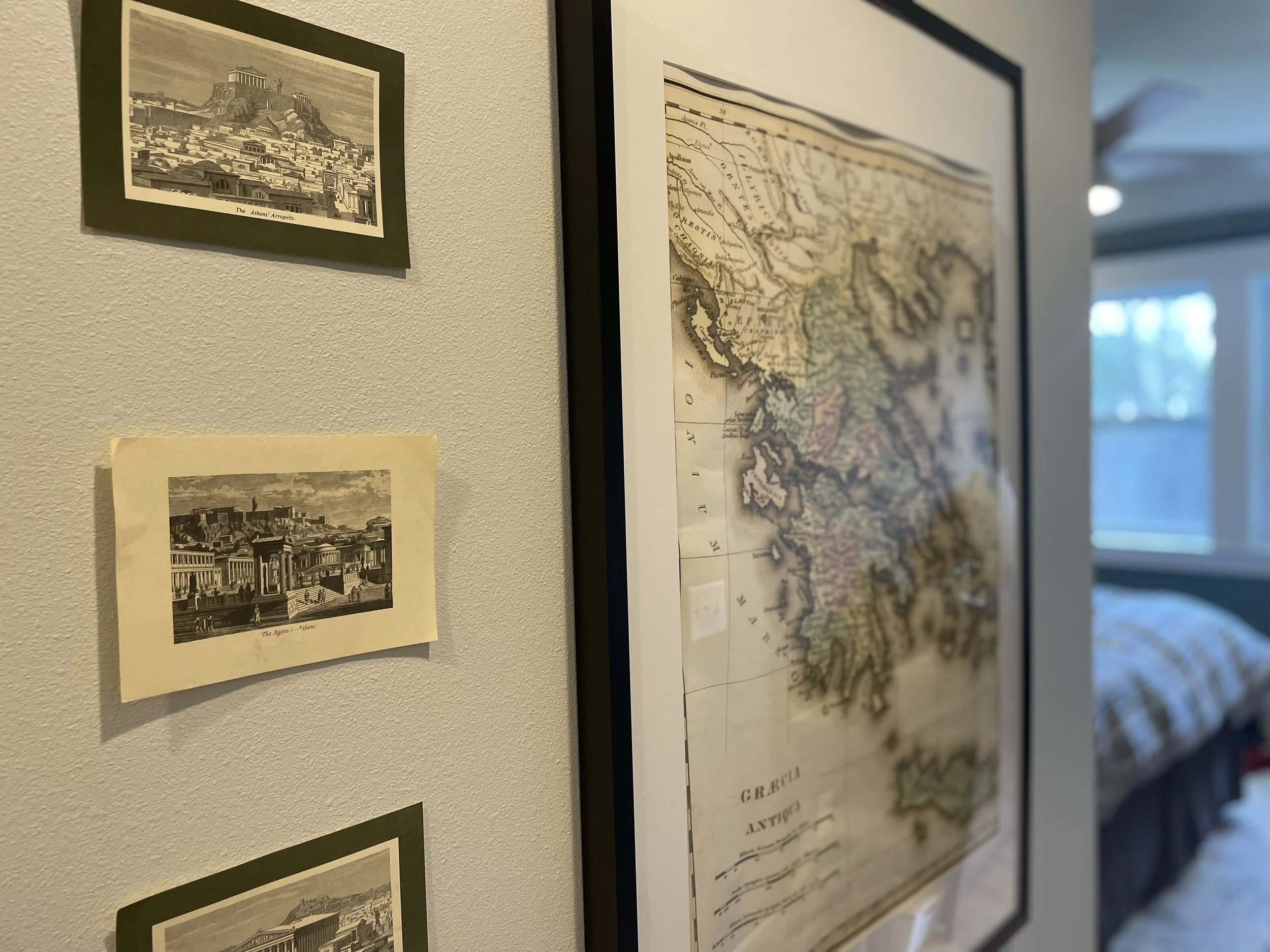 A section of a wall with three vintage-style black-and-white prints of historic landmarks, and a framed vintage map of Greece.