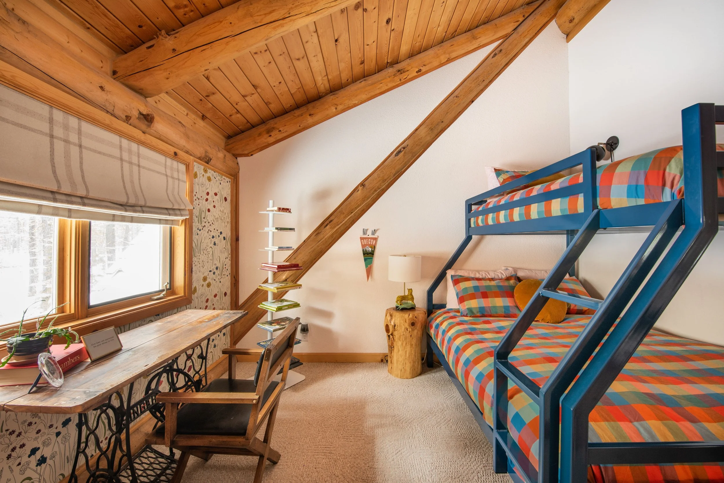 The cabin kids' bunk room features a teal metal bunk bed, vintage table, modern book stand, and curtains from The Shade Store.
