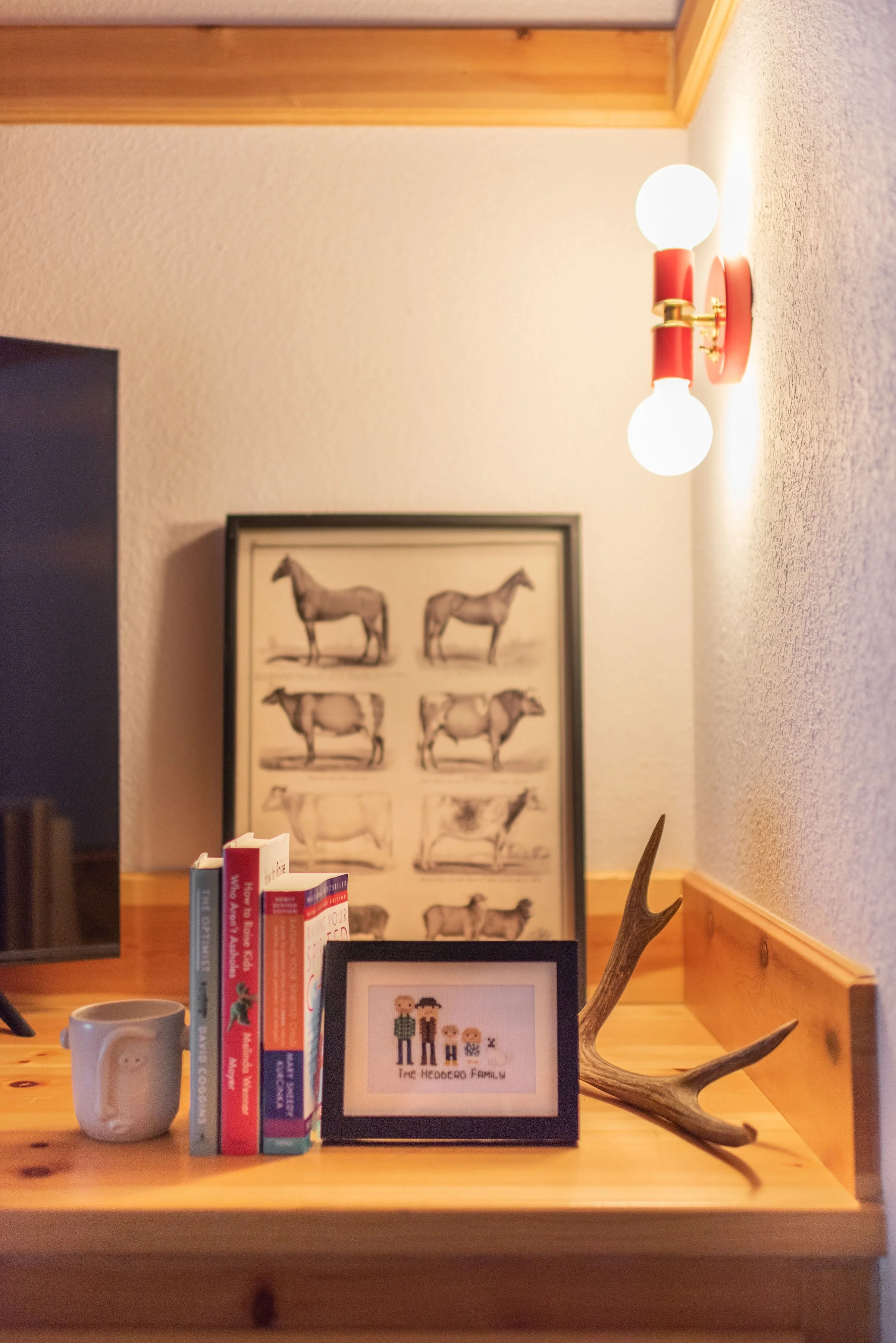 In the primary bedroom, we styled the shelf with modern cabin decor including antlers and a sewn family photo. The glow comes from a beautiful red and gold sconce from Sazerac Stitches.