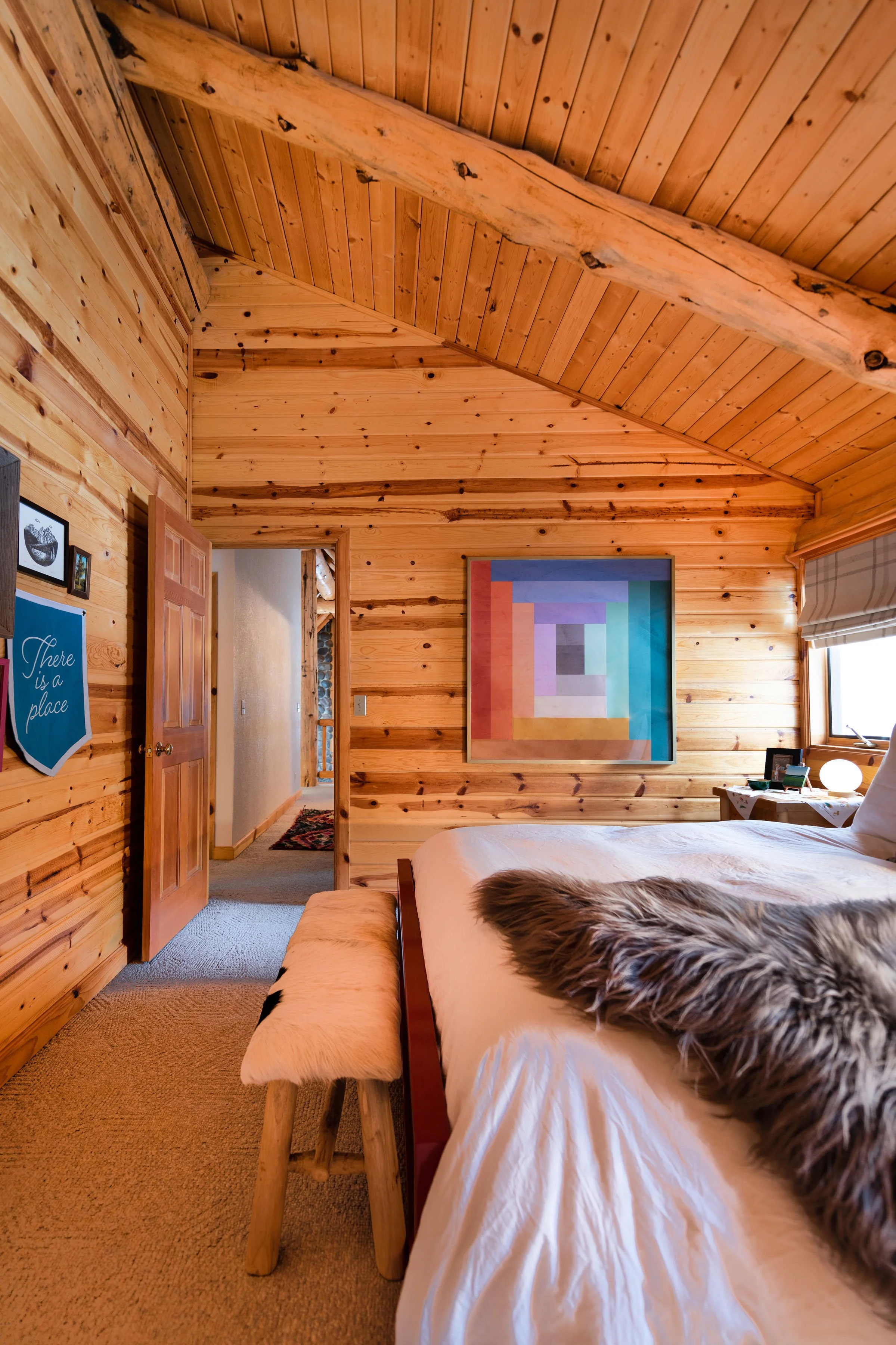 One of two guest bedrooms features a large modern quilt print, since quilting is a thing in Sisters, Oregon. It's paired with a red metal bedframe from Room & Board to pop against the log walls, and a fur throw blanket to add texture.