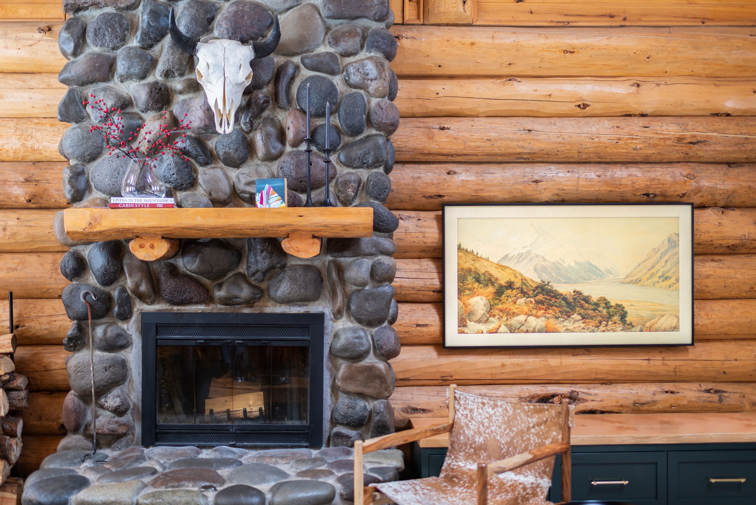 The stone fireplace features a hearth made out of logs, with a Frame TV by Samsung to the right that looks like a painting to blend in with the aesthetic.