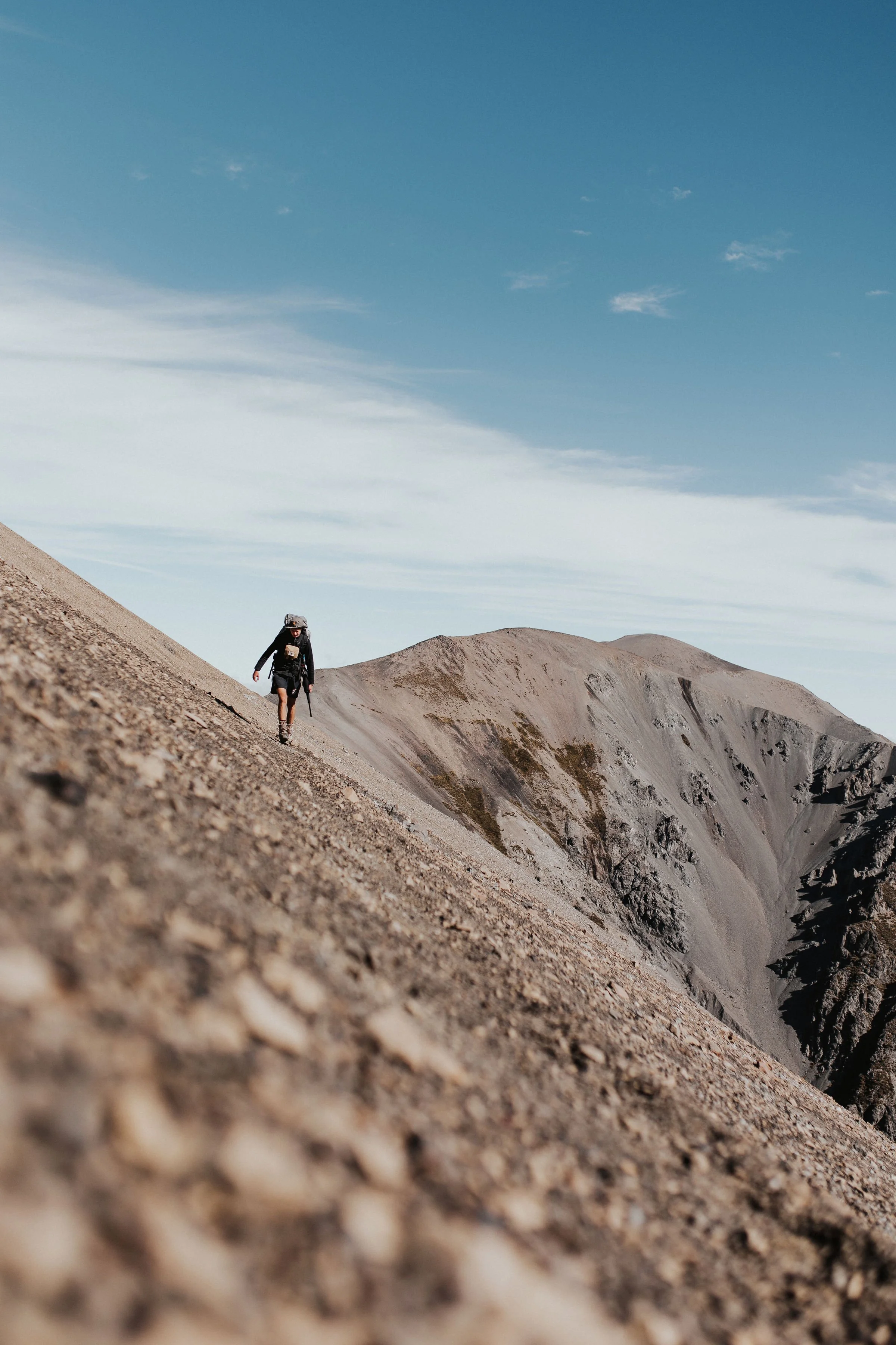 A person hiking on a steep, rocky mountain trail beneath a partly cloudy sky.