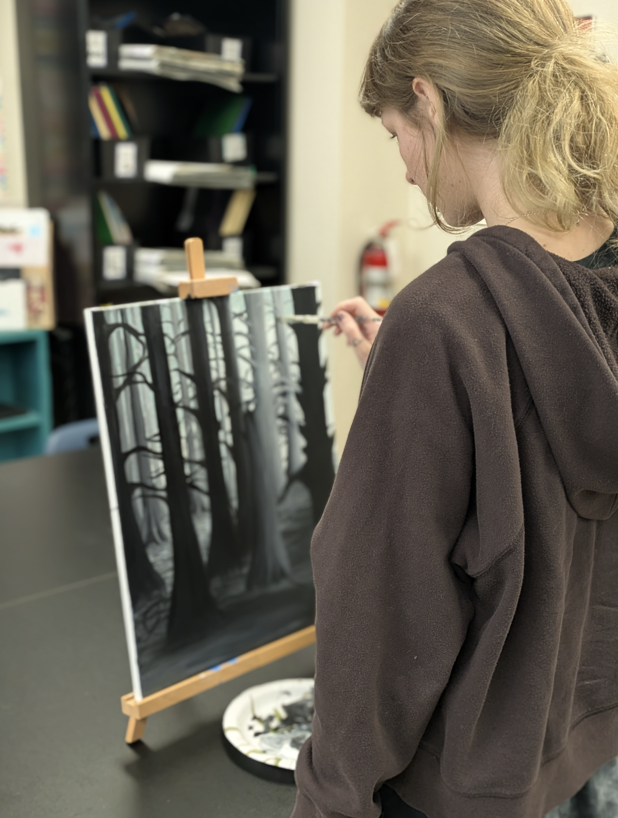 Student painting a black-and-white forest scene on canvas at Paint Away art studio