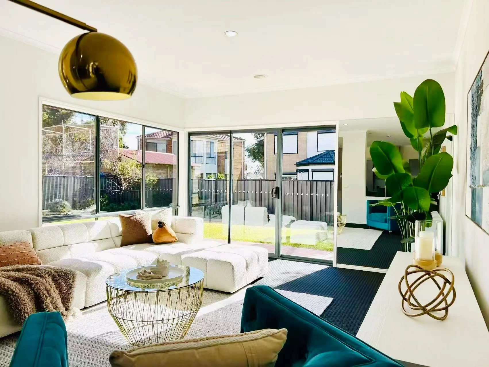 Cozy bedroom corner with a wooden chair, ornate gold mirror, indoor plant, colorful rug, open door, and white walls.