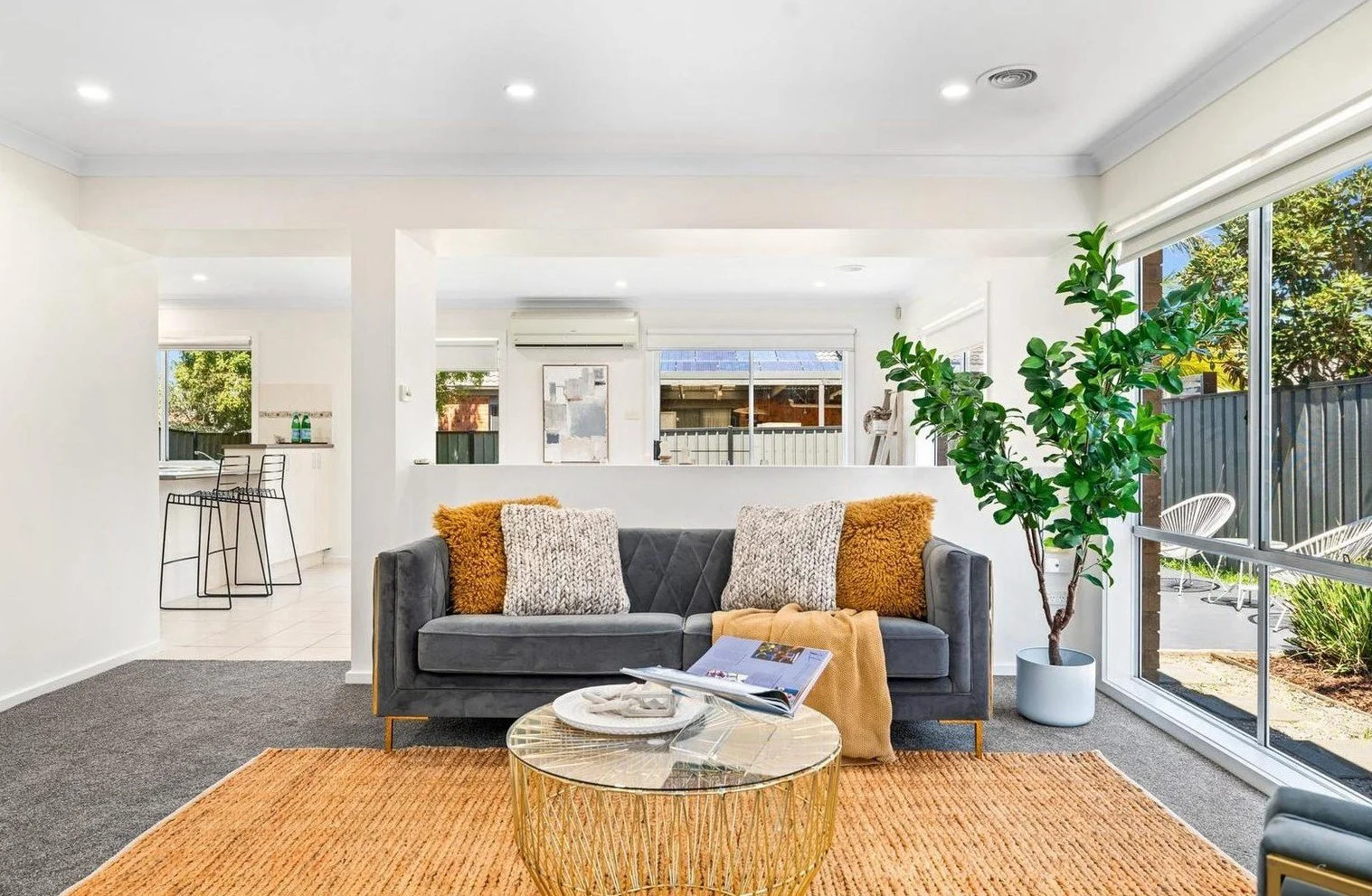 Modern living room with gray sofa, patterned cushions, abstract wall art, potted monstera plant, and a round coffee table.
