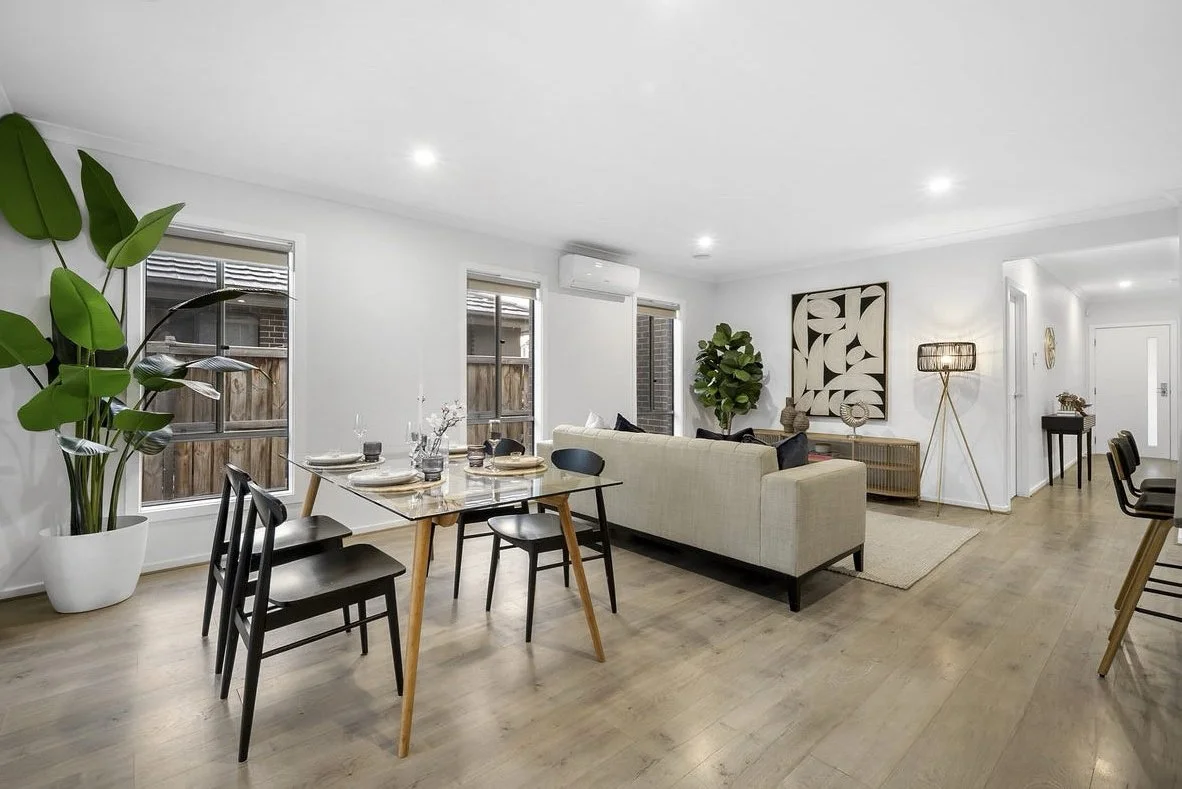 Modern dining room with glass table, six gray chairs, decorative vase, and wall art, adjacent to large sliding glass doors and a kitchen counter.