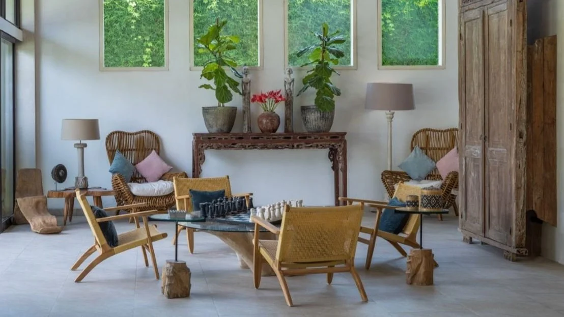 Living room with natural decor, wicker and wooden furniture, potted plants, lamps, and a chess set on a glass coffee table.