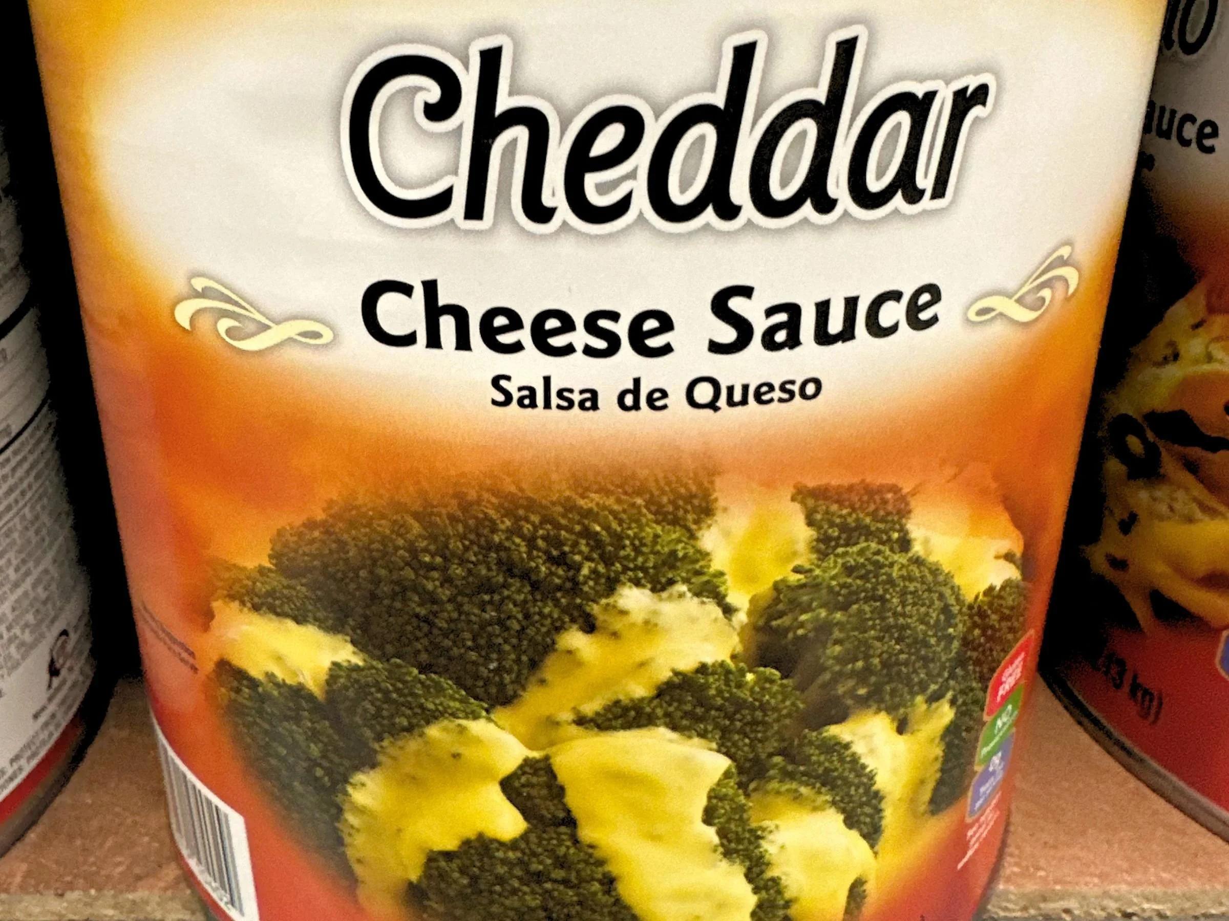 A photograph of a food-service sized can of cheddar cheese sauce which features an image of broccoli covered with melted cheese.