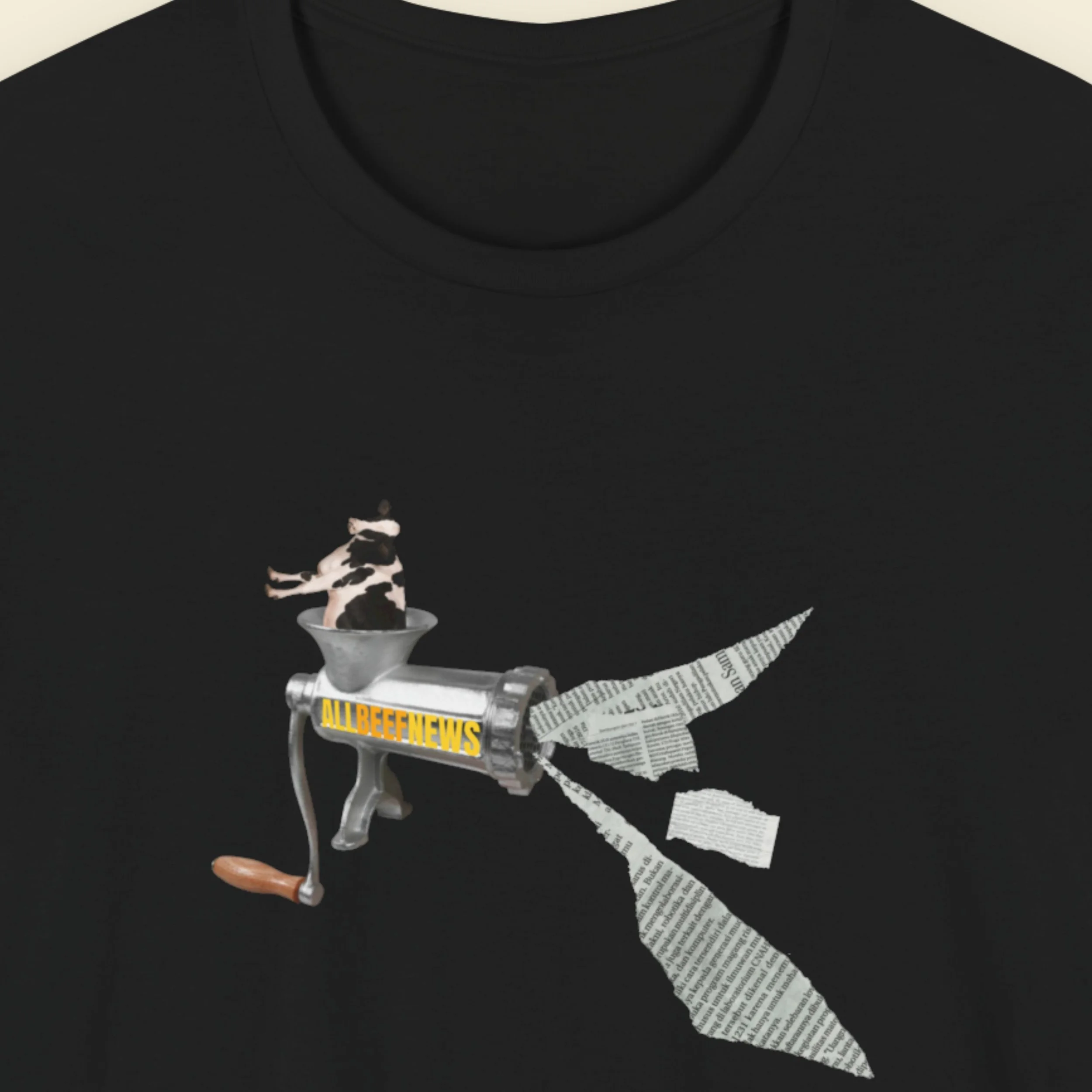 Black t-shirt with a fun, colorful cow in a meat grinder cartoon illustration on a beige background.