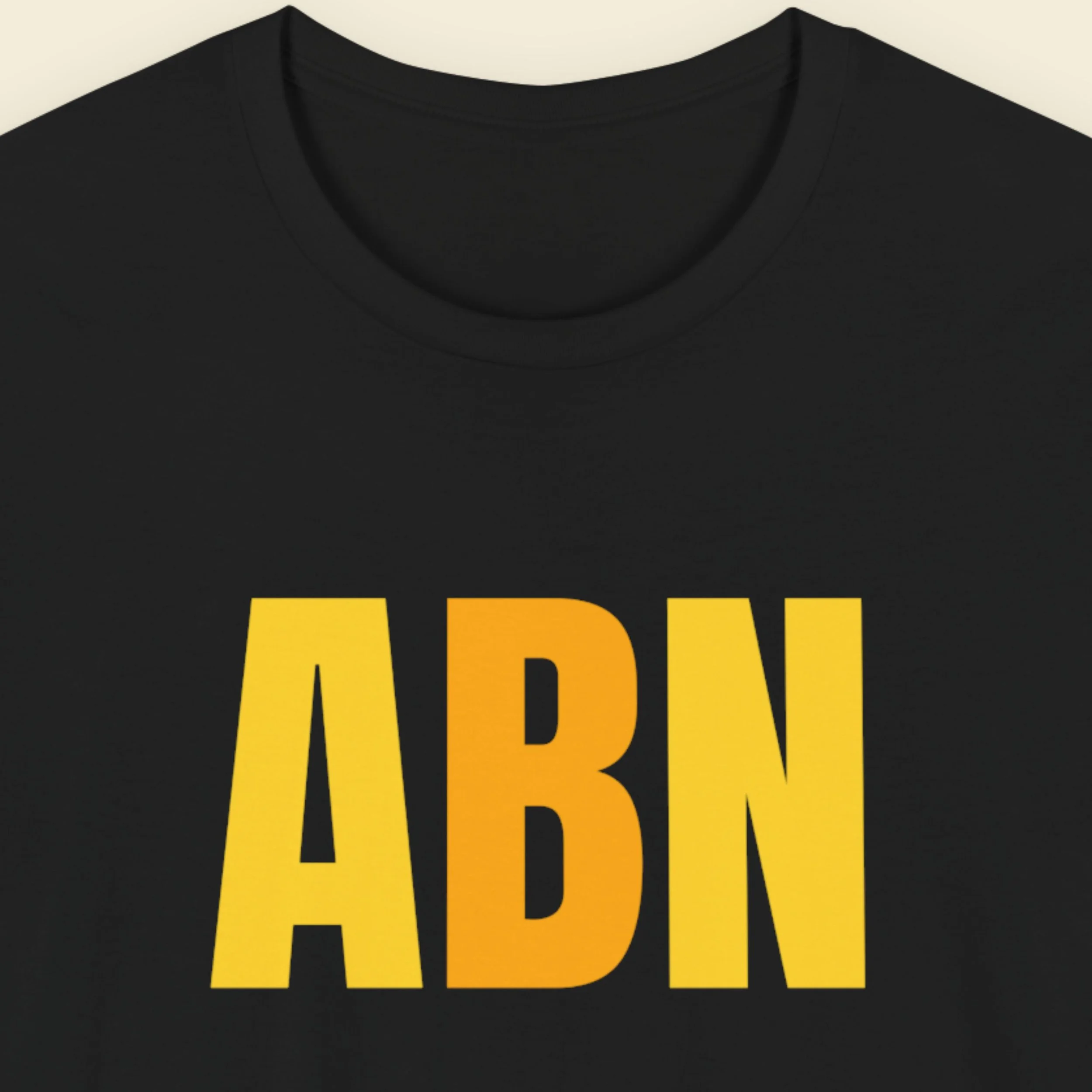A closeup image of a black t-shirt featuring a logo from satrical publication ALLBEEFNEWS the logo is the uppercase letters 'ABN' in yellow and orange.