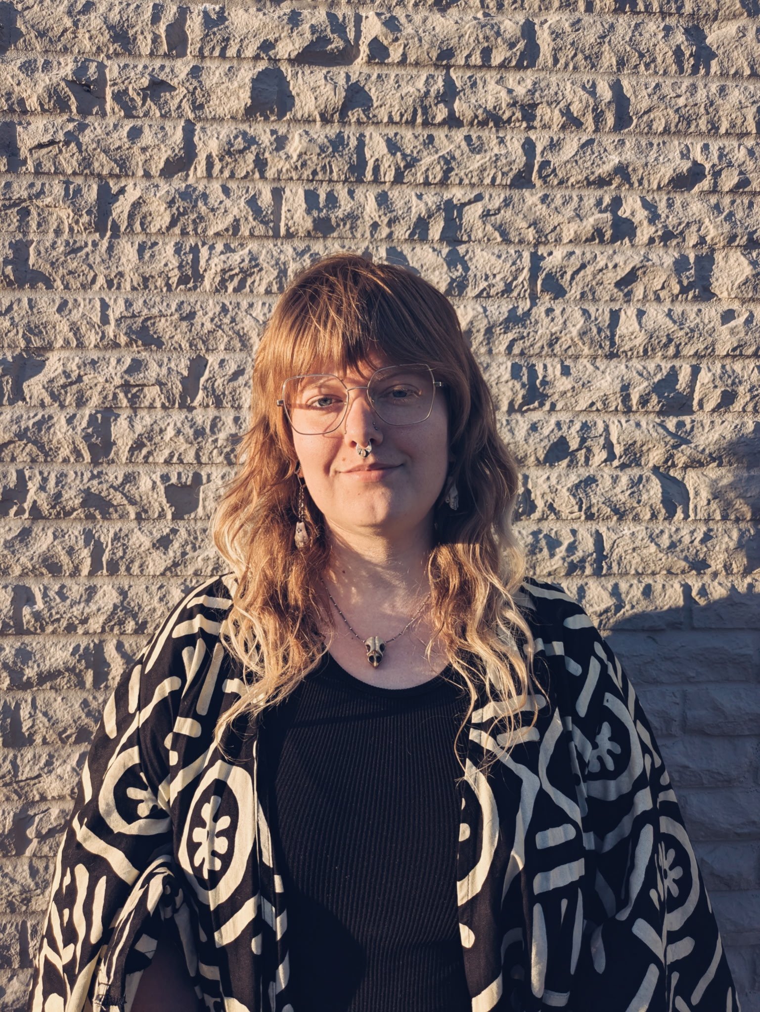 A smiling woman with short dark hair sitting at an outdoor table with a flower arrangement in a glass vase nearby.
