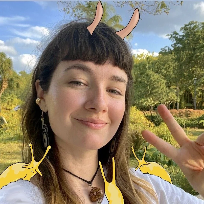 A young woman with braided blue hair smiling and making a peace sign, with cartoon yellow bananas superimposed around her