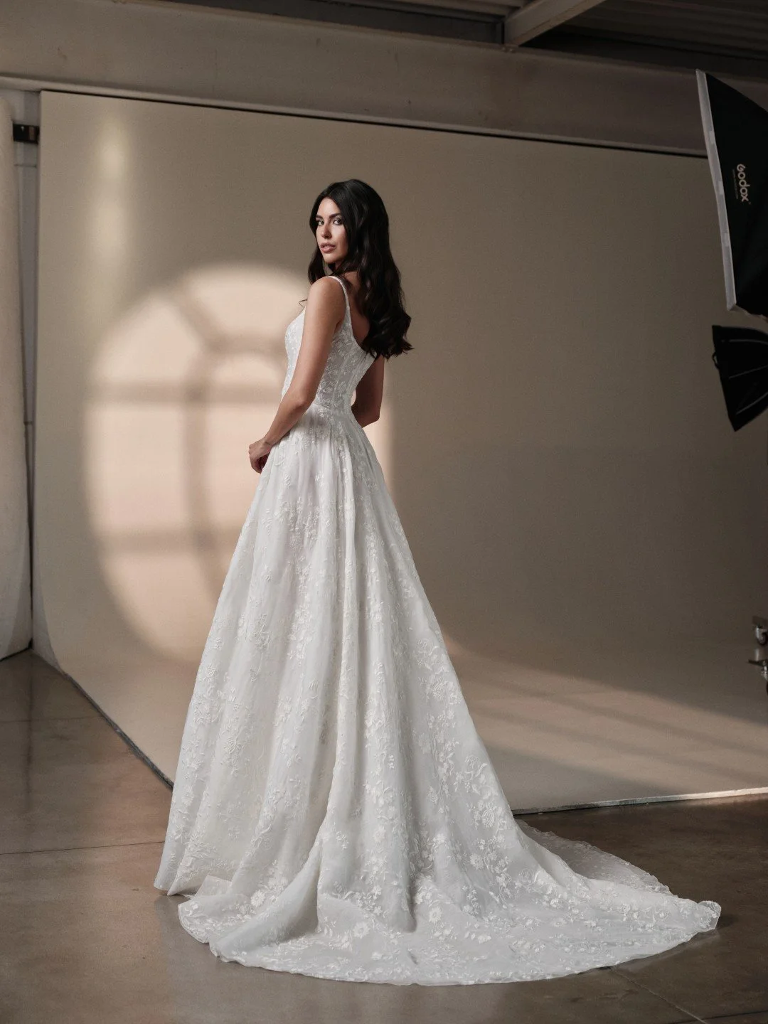 Maria Pia at New York Bridal Market.  A woman in a white wedding gown standing in a photography studio with a beige backdrop and studio lights.