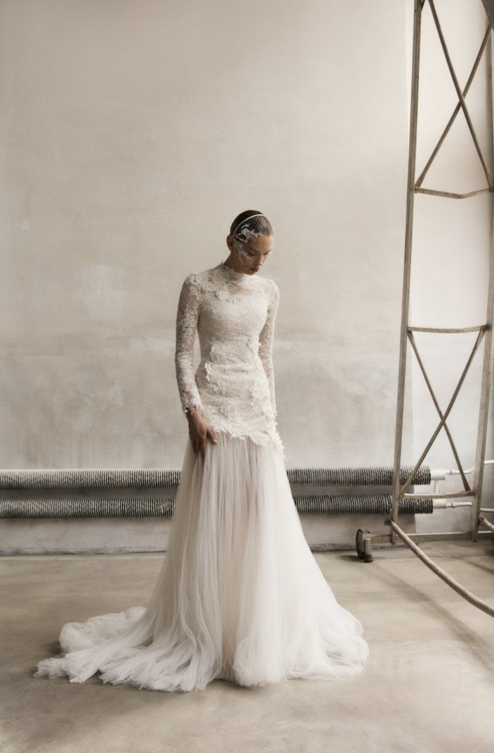 Marmar Halim at New York Bridal Market A woman wearing a long, elegant wedding dress with lace top and flowing skirt, standing alone against a plain background.