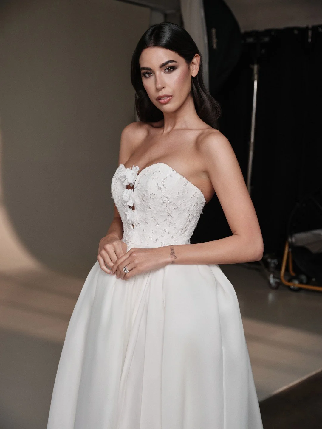 Maria Pia at New York Bridal Market.  A woman in a white wedding dress with a strapless lace bodice and a full skirt, standing in a photography studio.